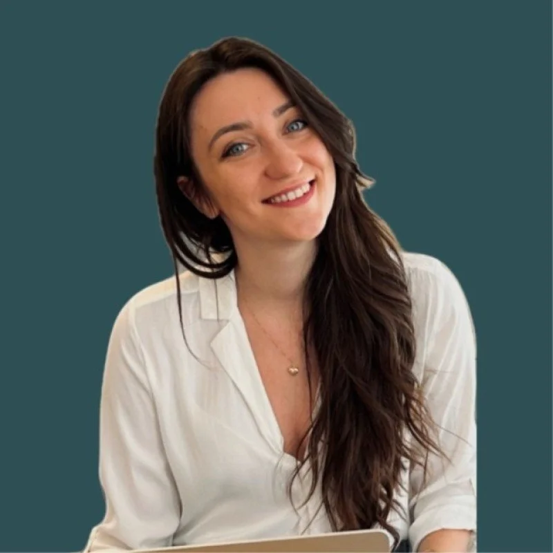 A smiling woman with long dark hair wearing a white blouse against a solid teal background.