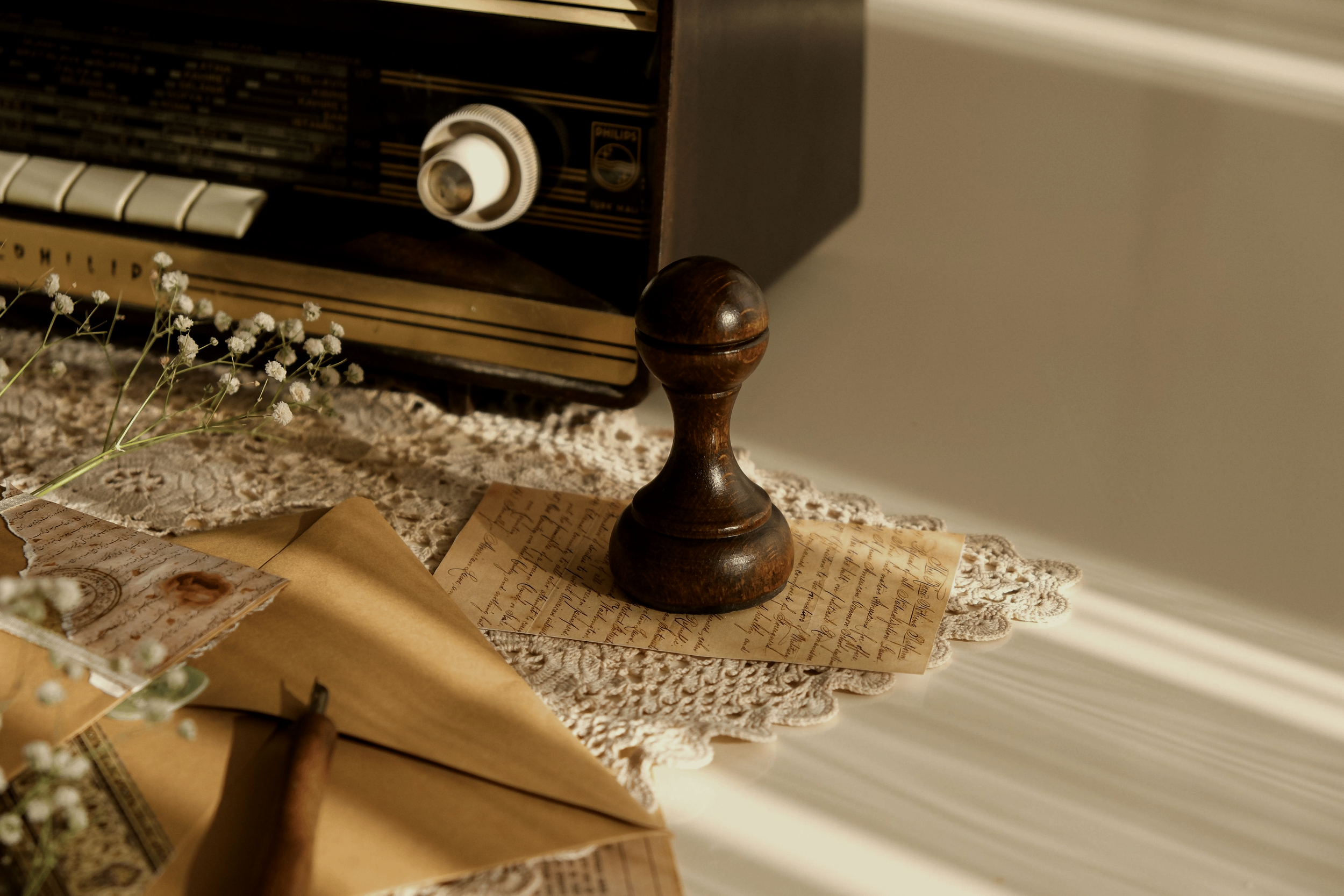 Vintage radio on a lace tablecloth, surrounded by handwritten letters, a stringed instrument, and dried flowers.