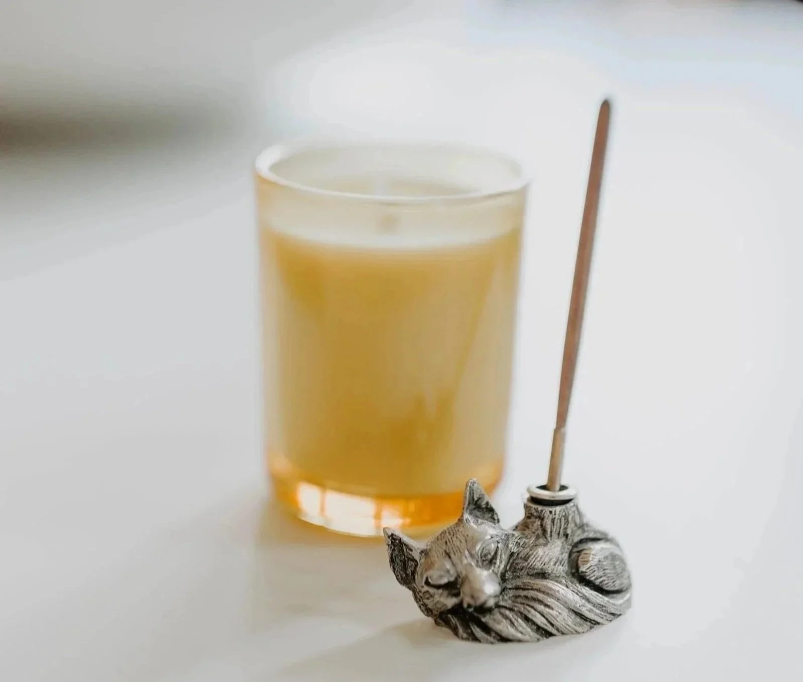 A candle with a meditative scent and a silver fox-shaped ink holder with a calligraphy pen.