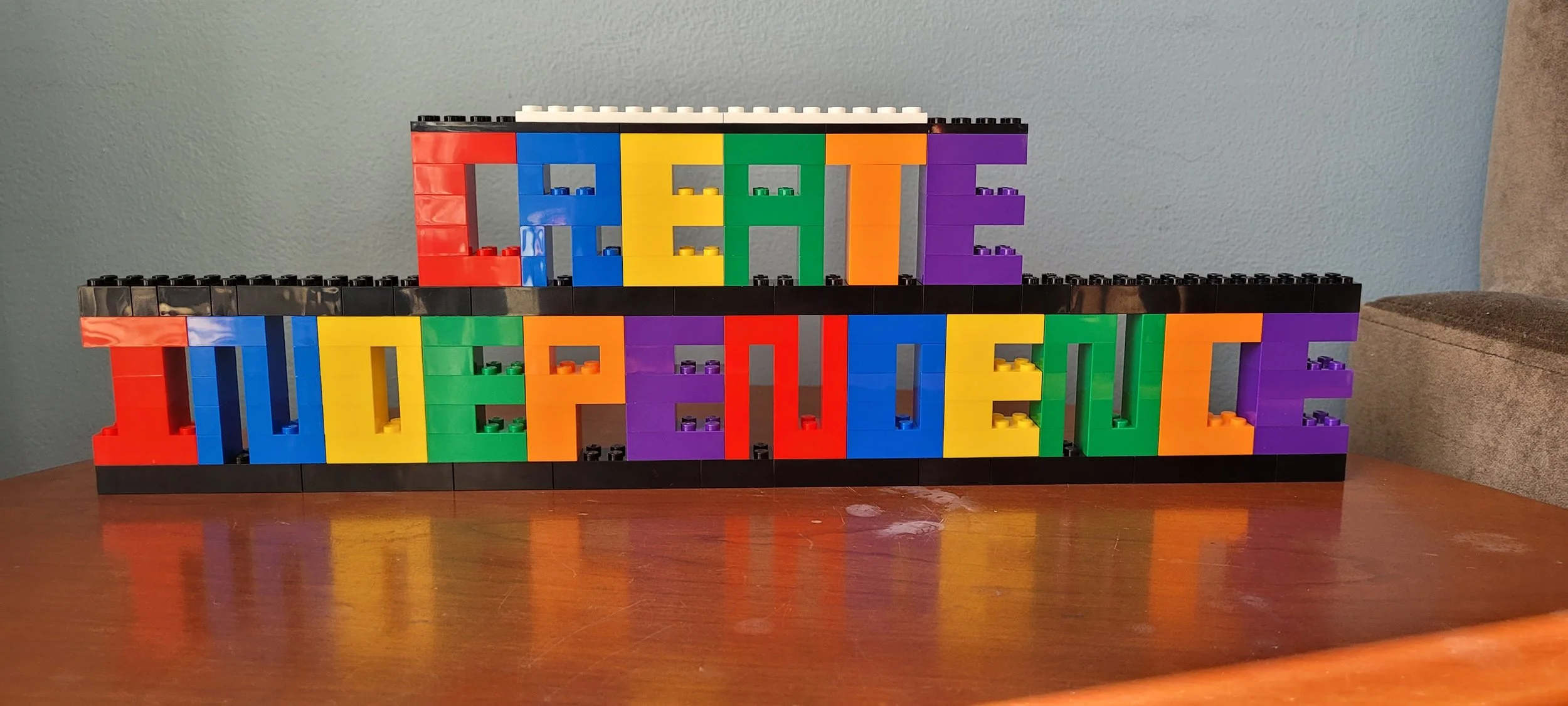 Colorful LEGO bricks spelling out 'CREATE THE POSSIBLE' on a wooden table against a light blue wall.