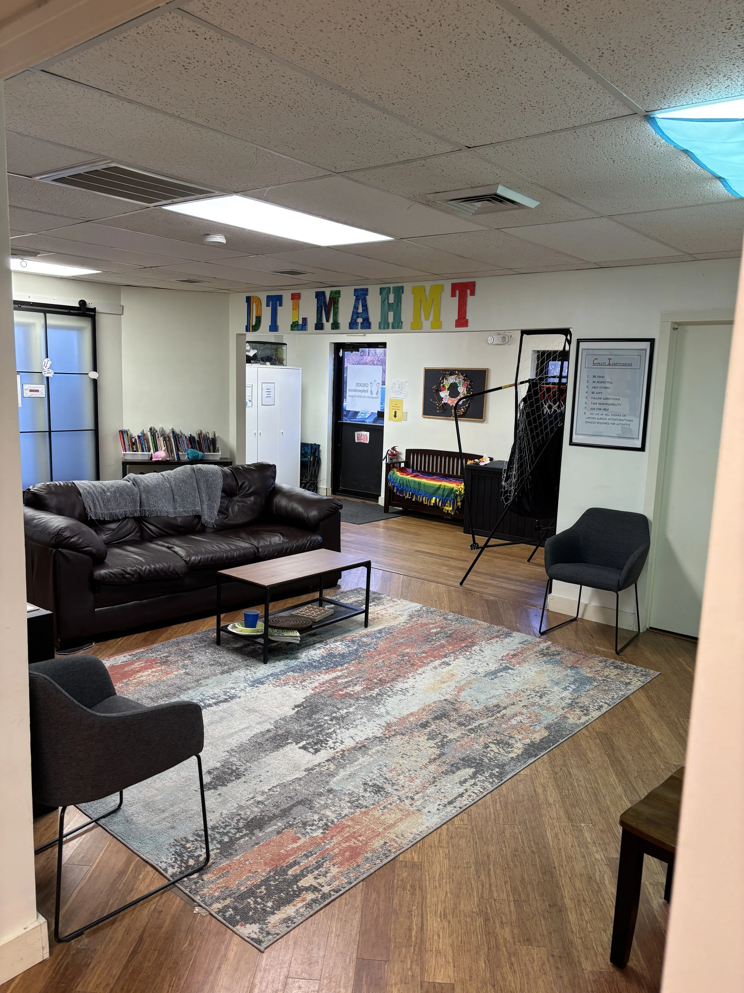 Comfortable waiting area with sofa, armchair, coffee table, and a rug, and a small bench with rainbow blanket, near a doorway with a rainbow-colored decoration.