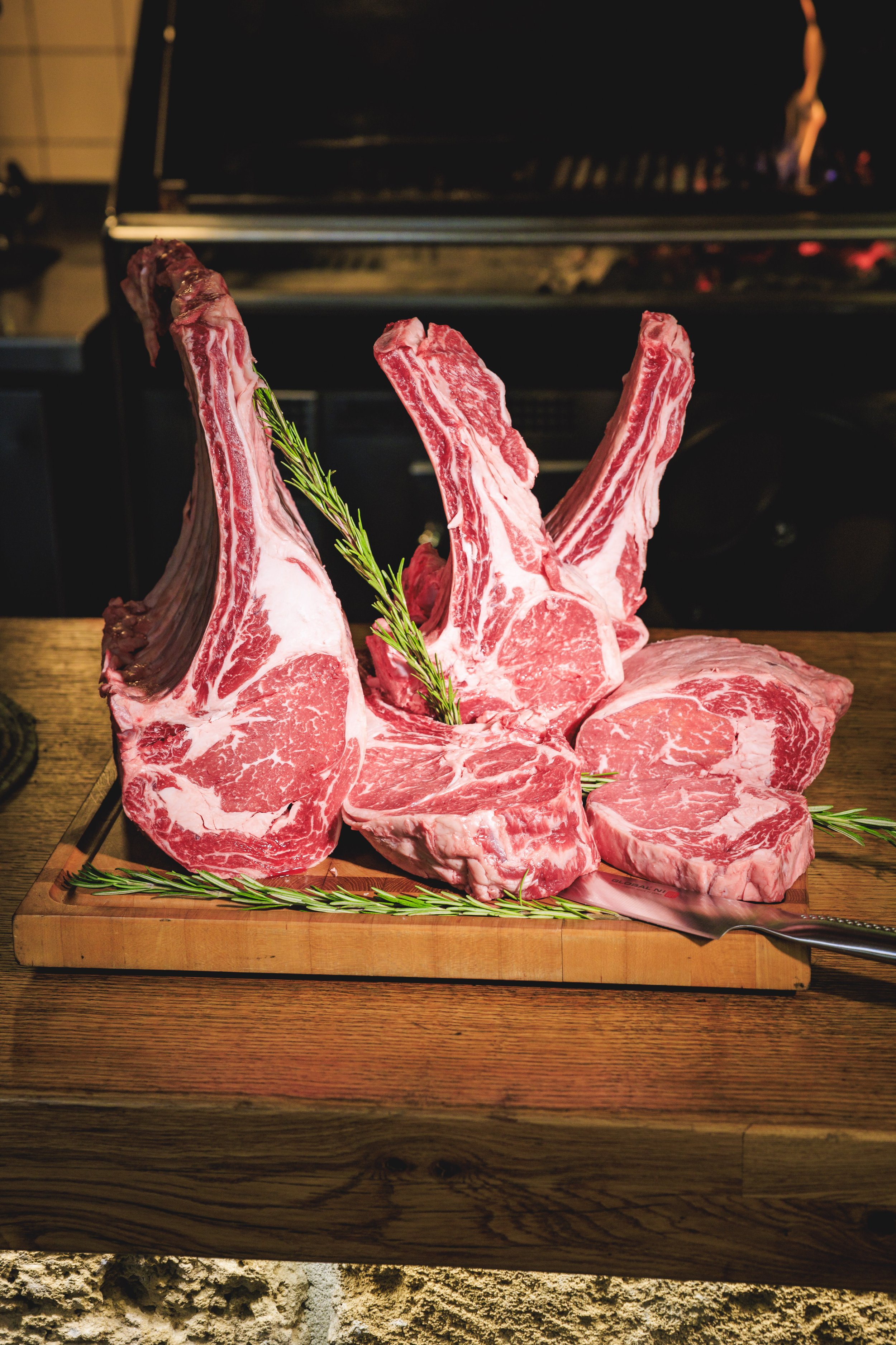 Raw beef steaks and ribeye cuts with sprigs of rosemary on a wooden cutting board.