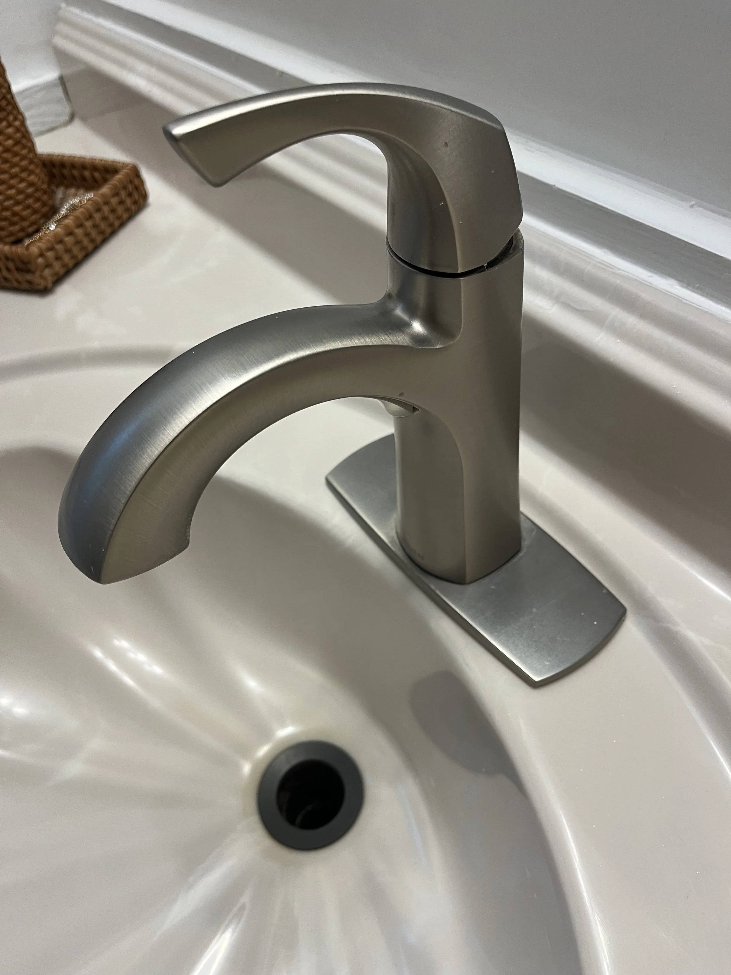 A brushed nickel bathroom faucet mounted on a white sink with a drain at the bottom.