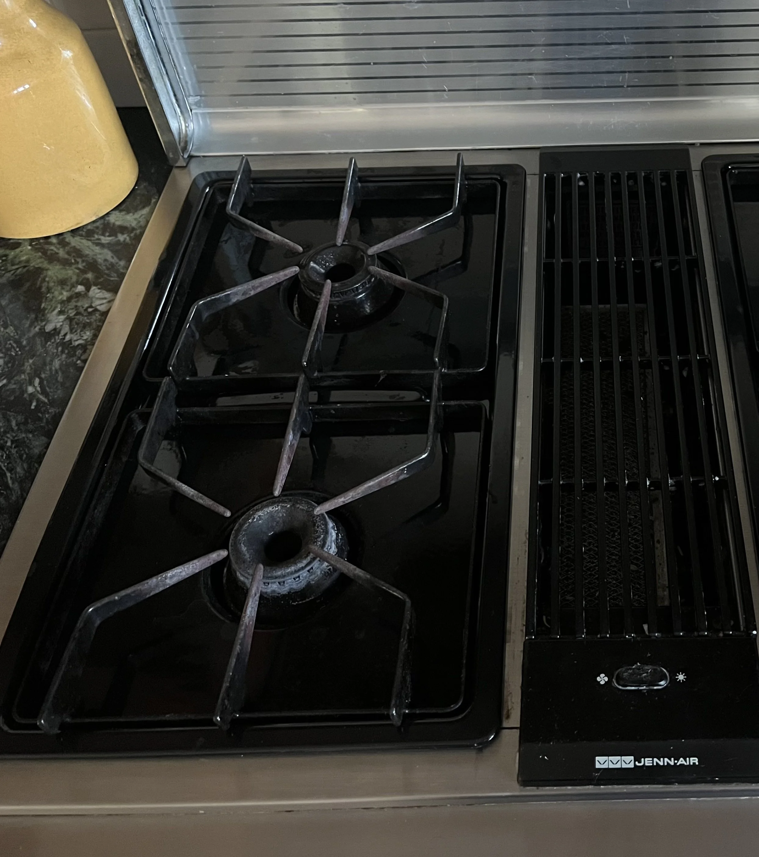 A stovetop with two gas burners, one slightly larger than the other, with black grates and control knobs on the right side, labeled Jenn-Air.