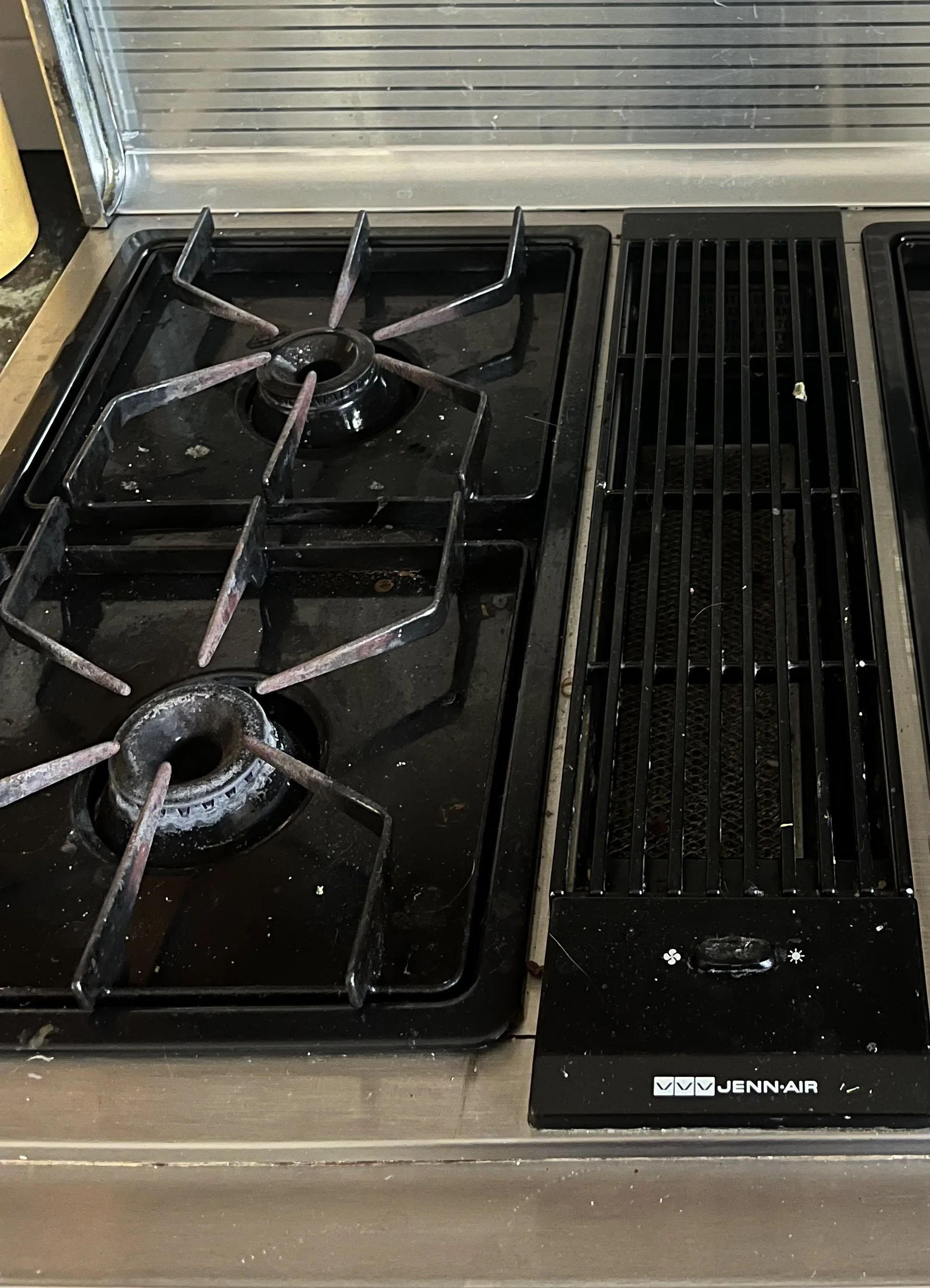 Dirty stovetop with two burners and a grill.