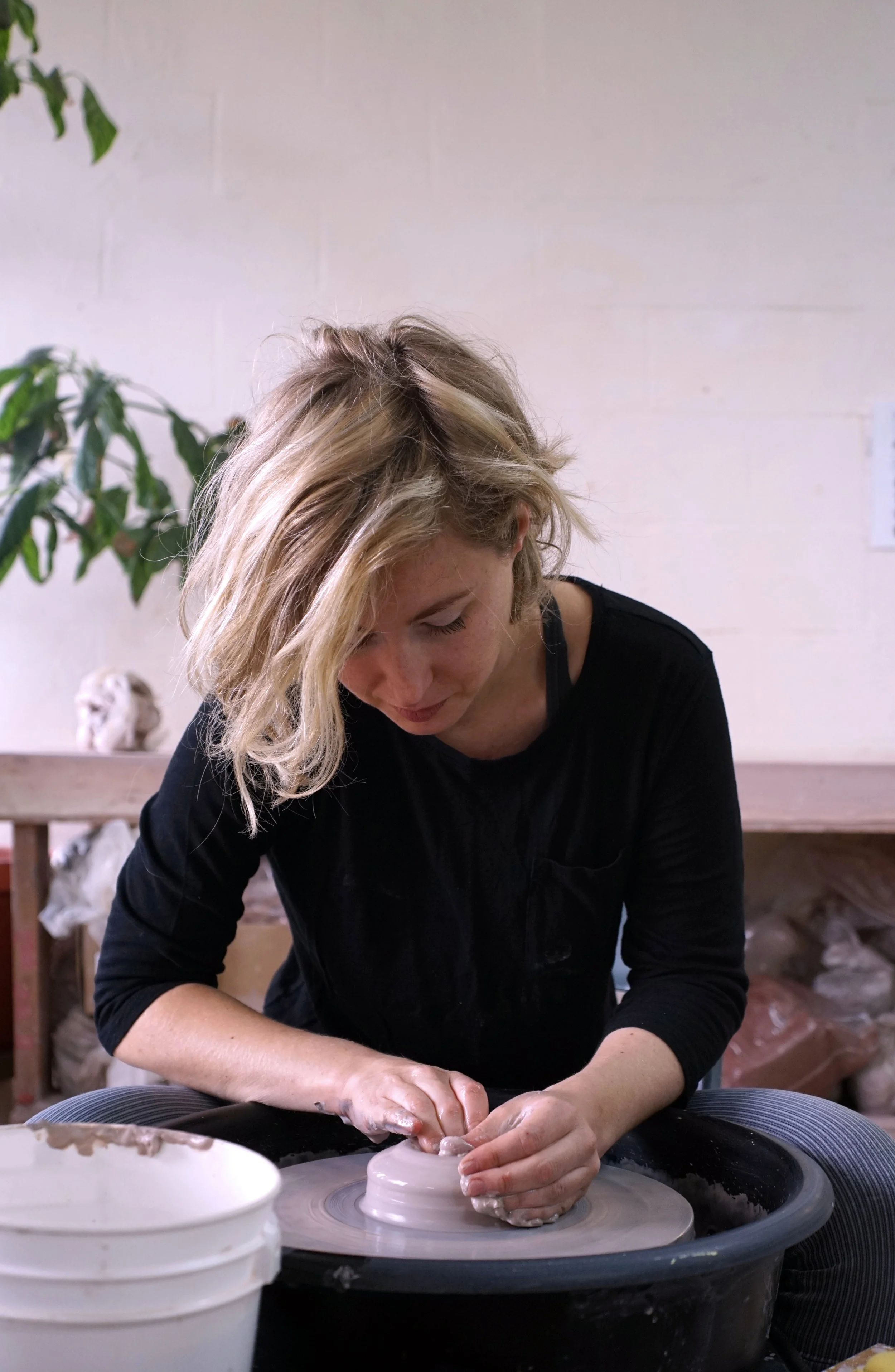 Zuzka Vaclavik shaping clay on a pottery wheel in a studio.