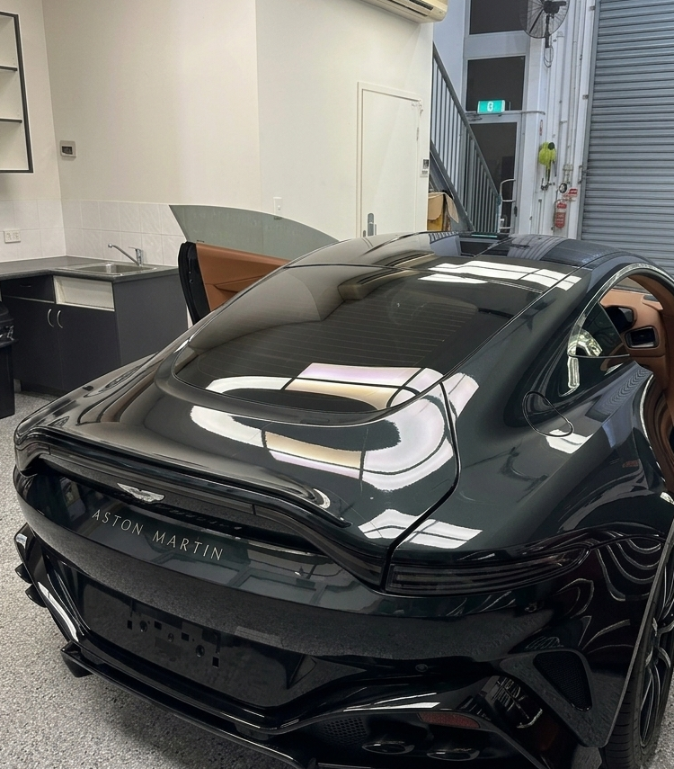 A black Aston Martin sports car with open driver and passenger side doors, parked indoors in a workshop or garage.