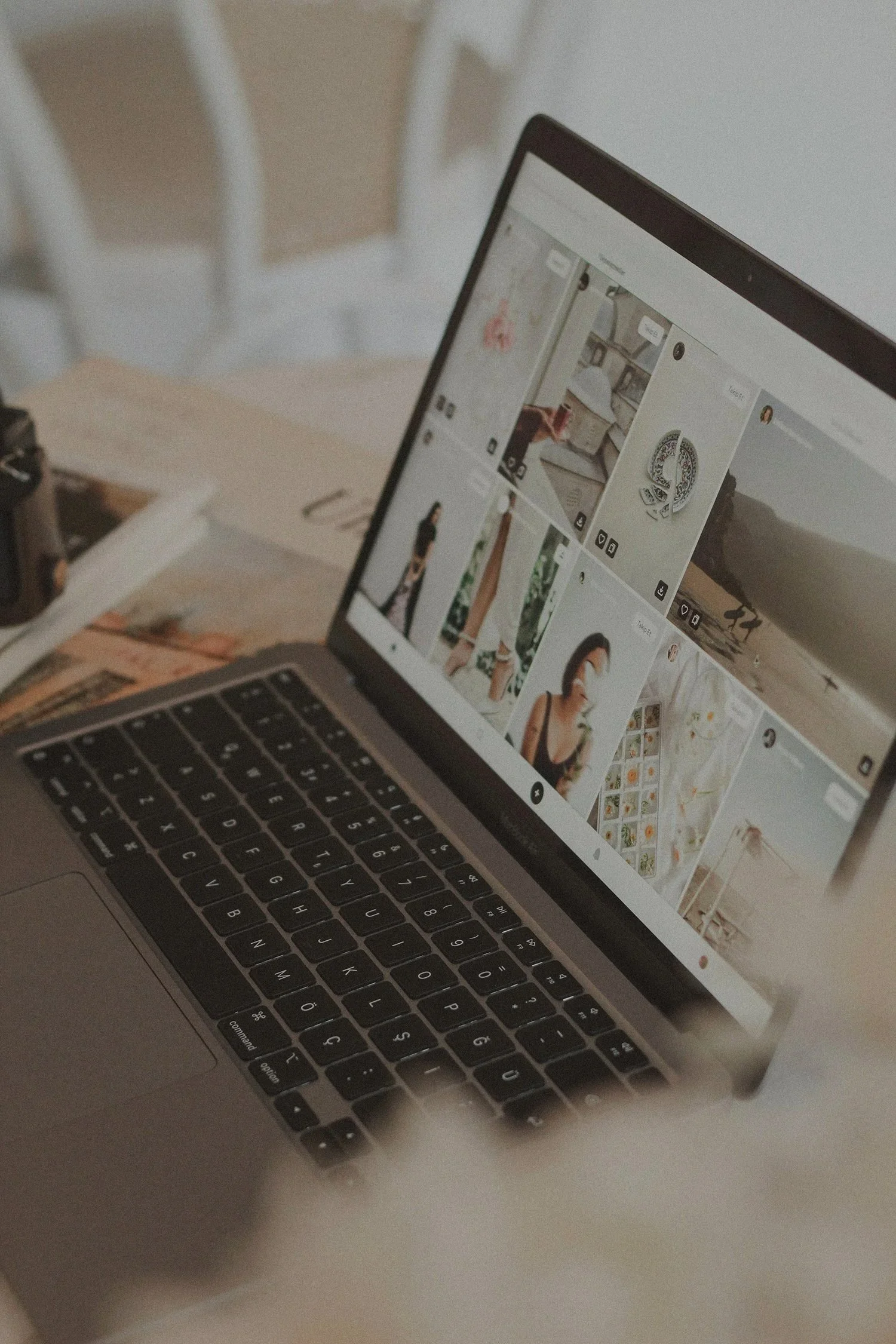 A laptop computer displaying a Pinterest feed, placed on a desk with a camera, a notepad, and a pen nearby.
