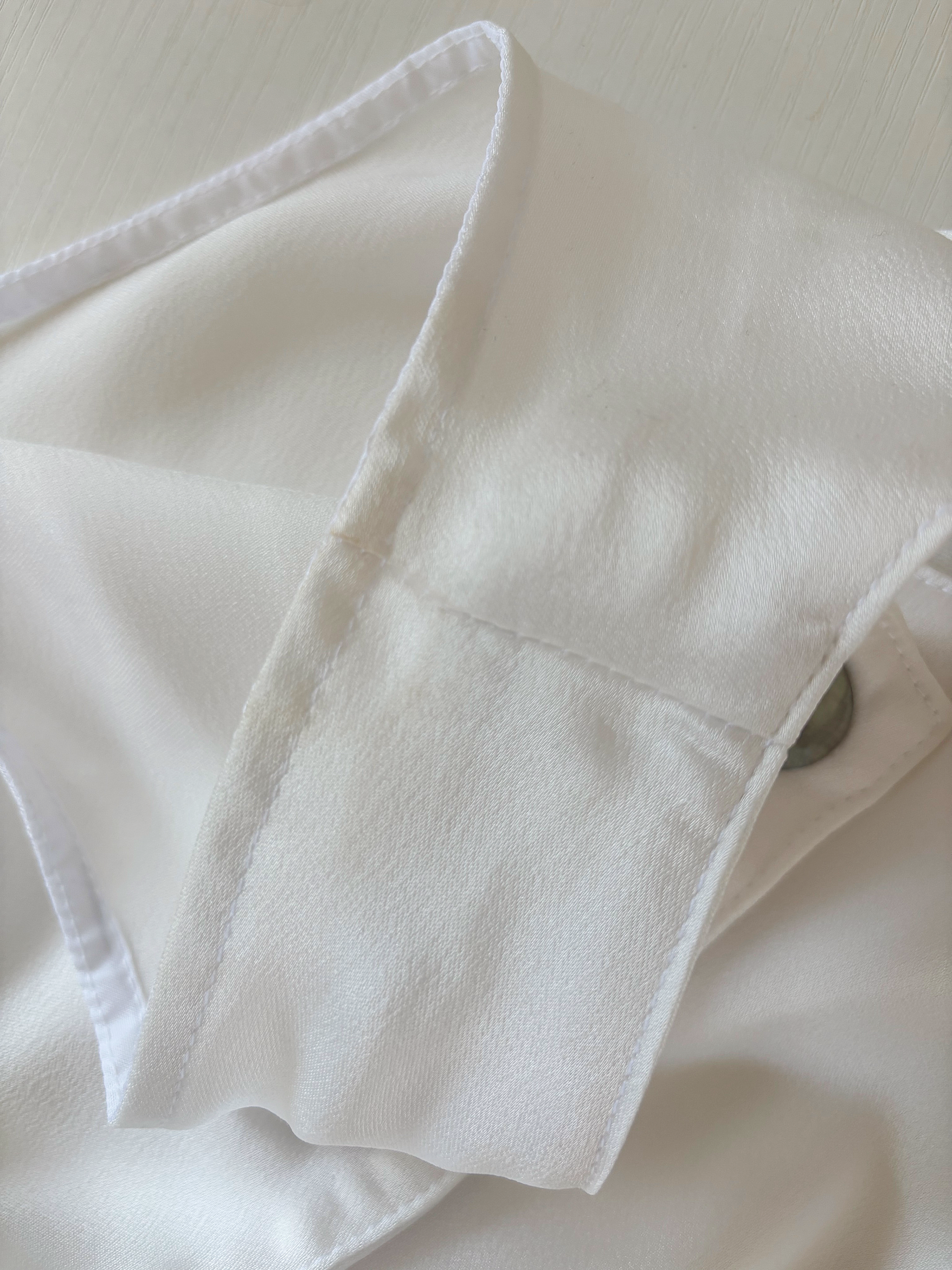 Close-up of a white satin dress with visible stitching and a hidden button.
