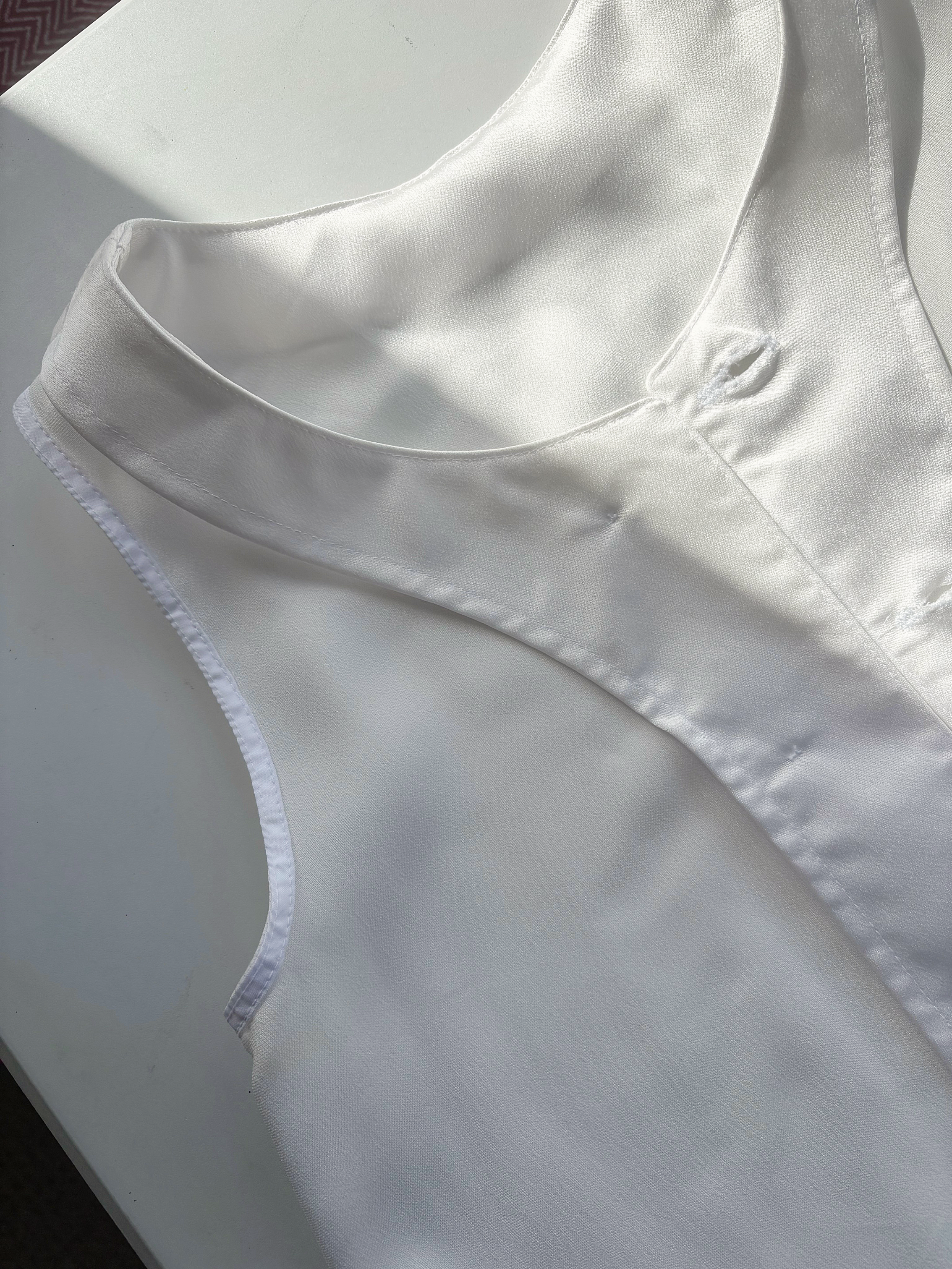 Reverse details of white satin dress and lapel on a white surface with natural light.