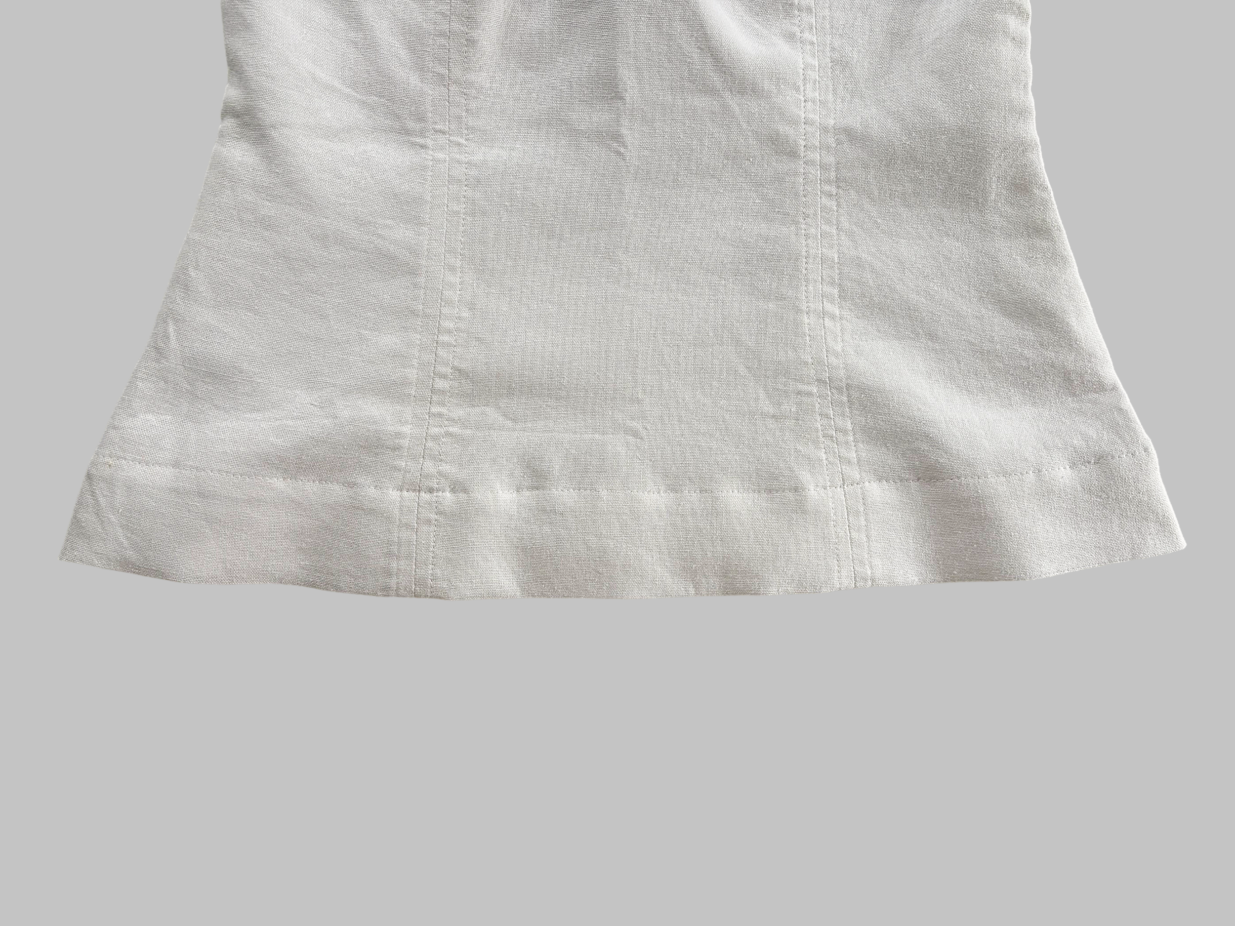 Close-up of linen top with visible hem stitching details, on a plain gray background.
