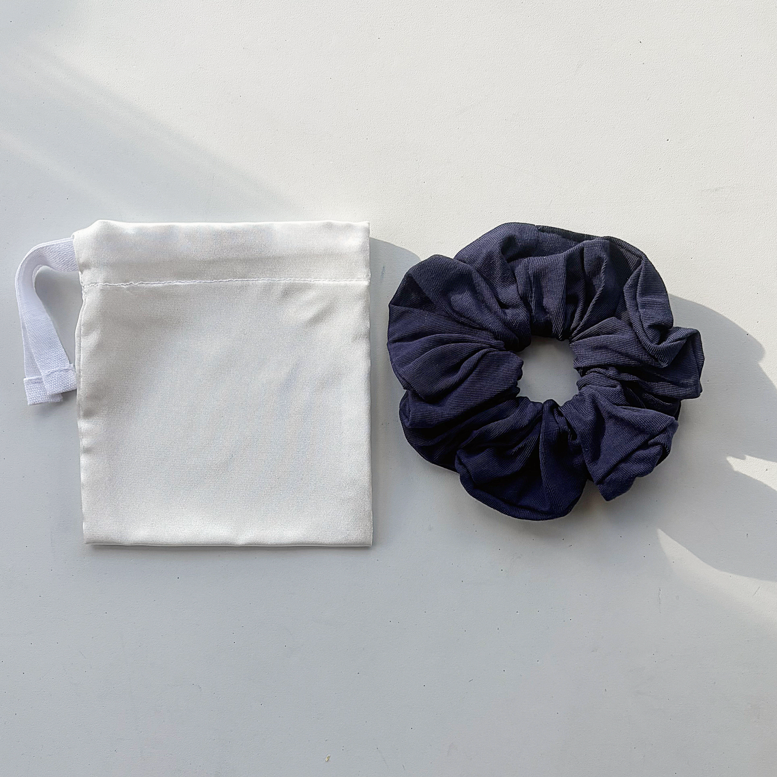 A white cloth face mask and a dark blue scrunchie placed on a white surface.
