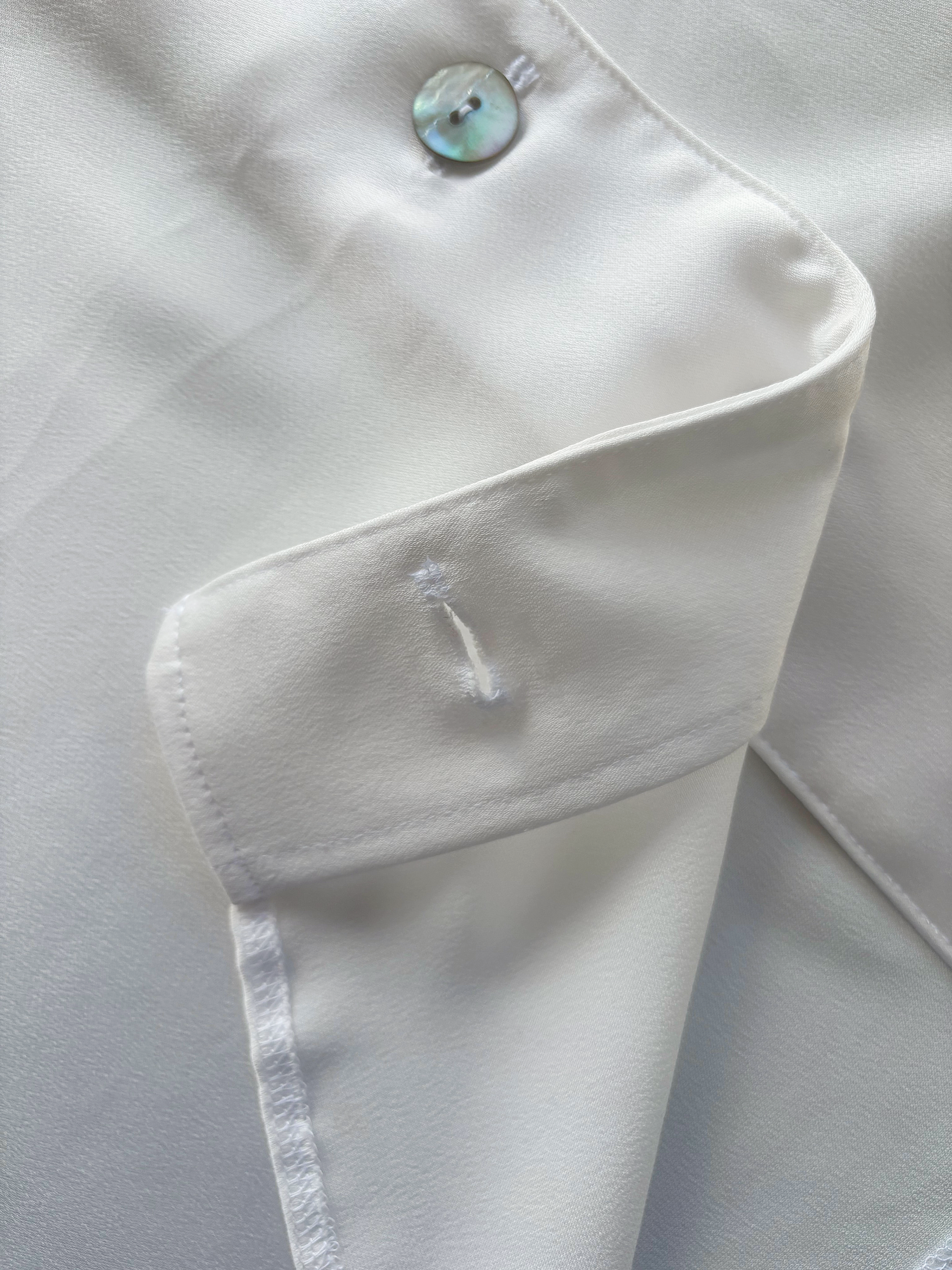 Close-up of a white satin dress with a button and a pocket.