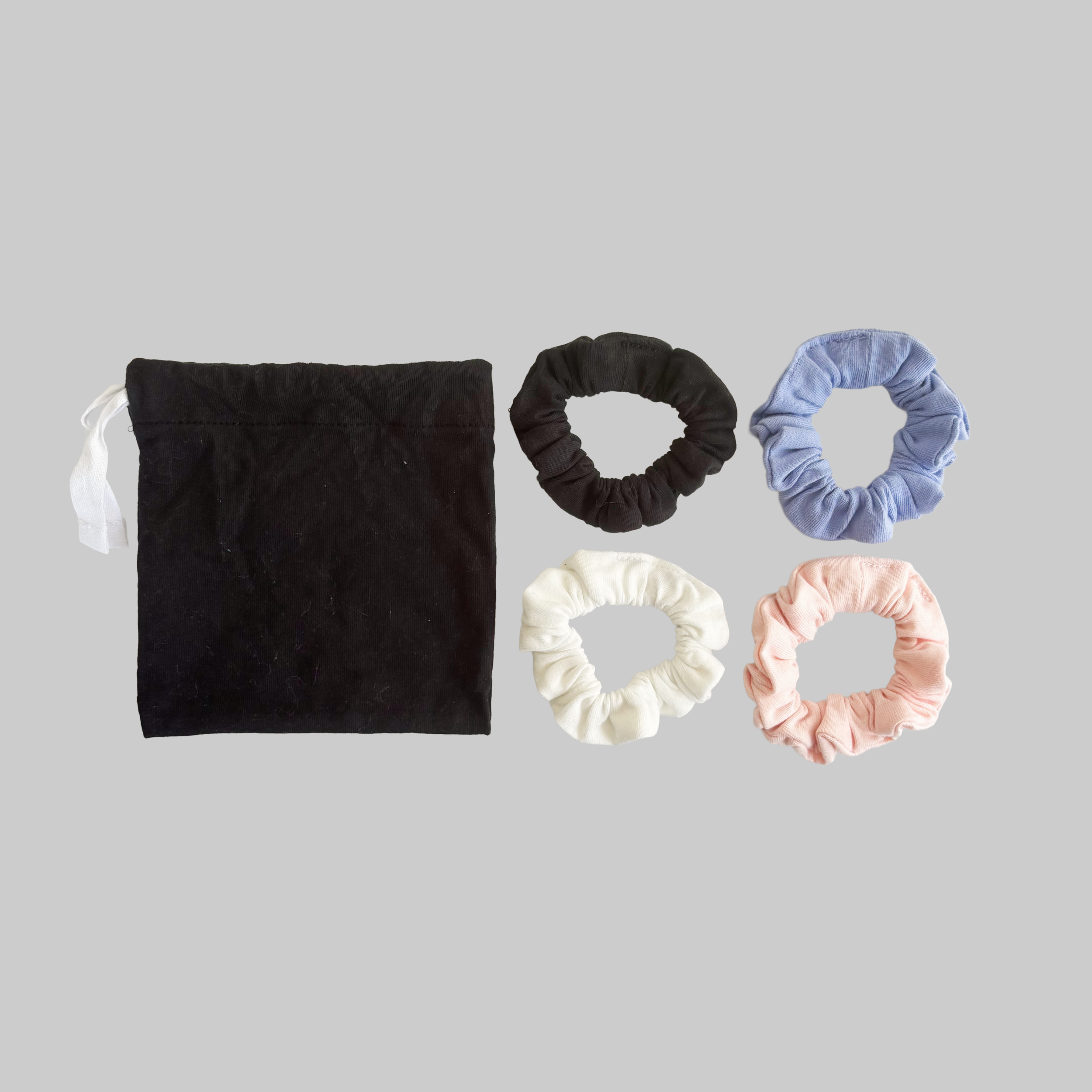 Close-up of six scrunchies made of different fabrics and colors, arranged against a light gray background.