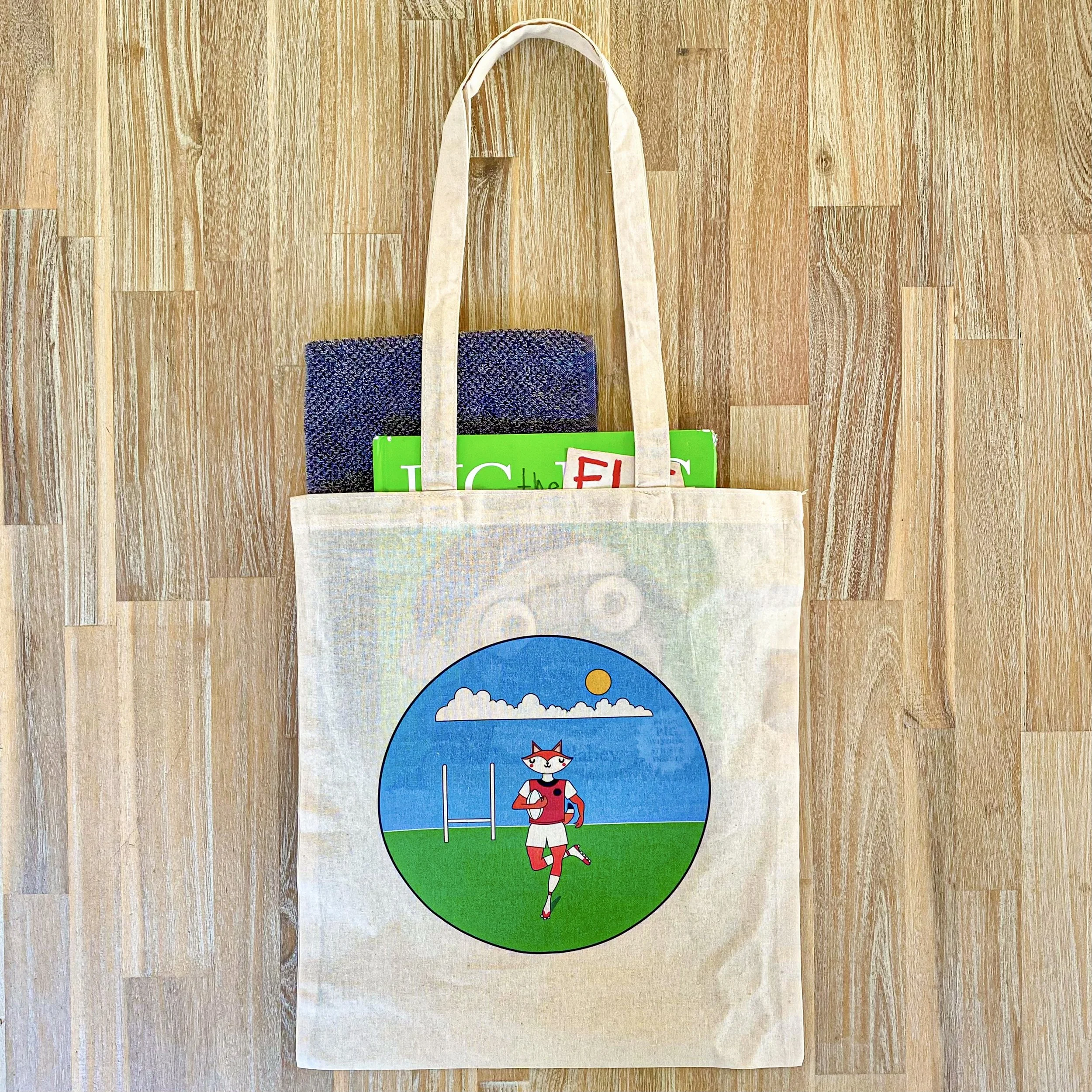 Photo of printed logo tote bag with picture books and a towel stacked into it.