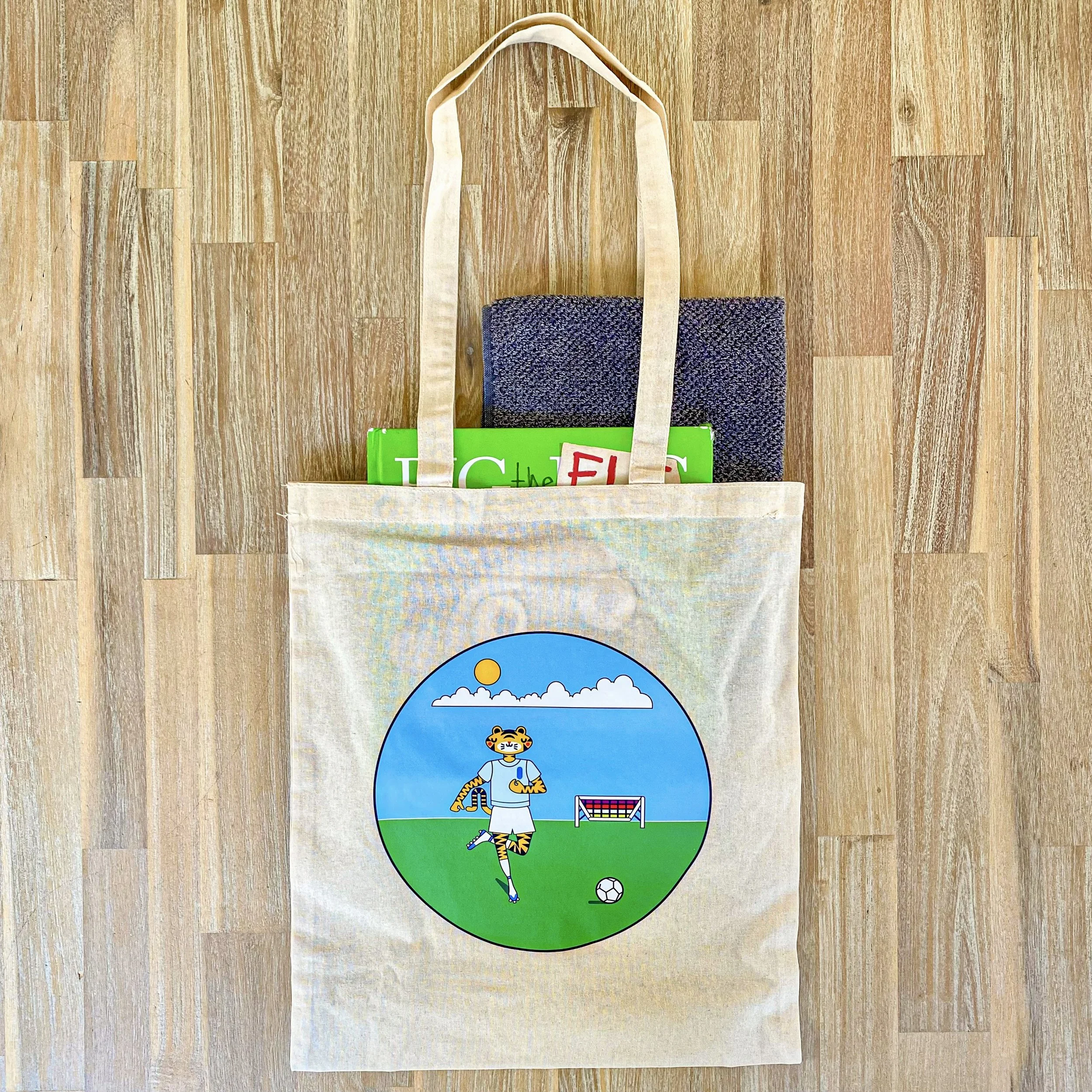 Photo of printed tote bag with picture books and a towel stacked into it.