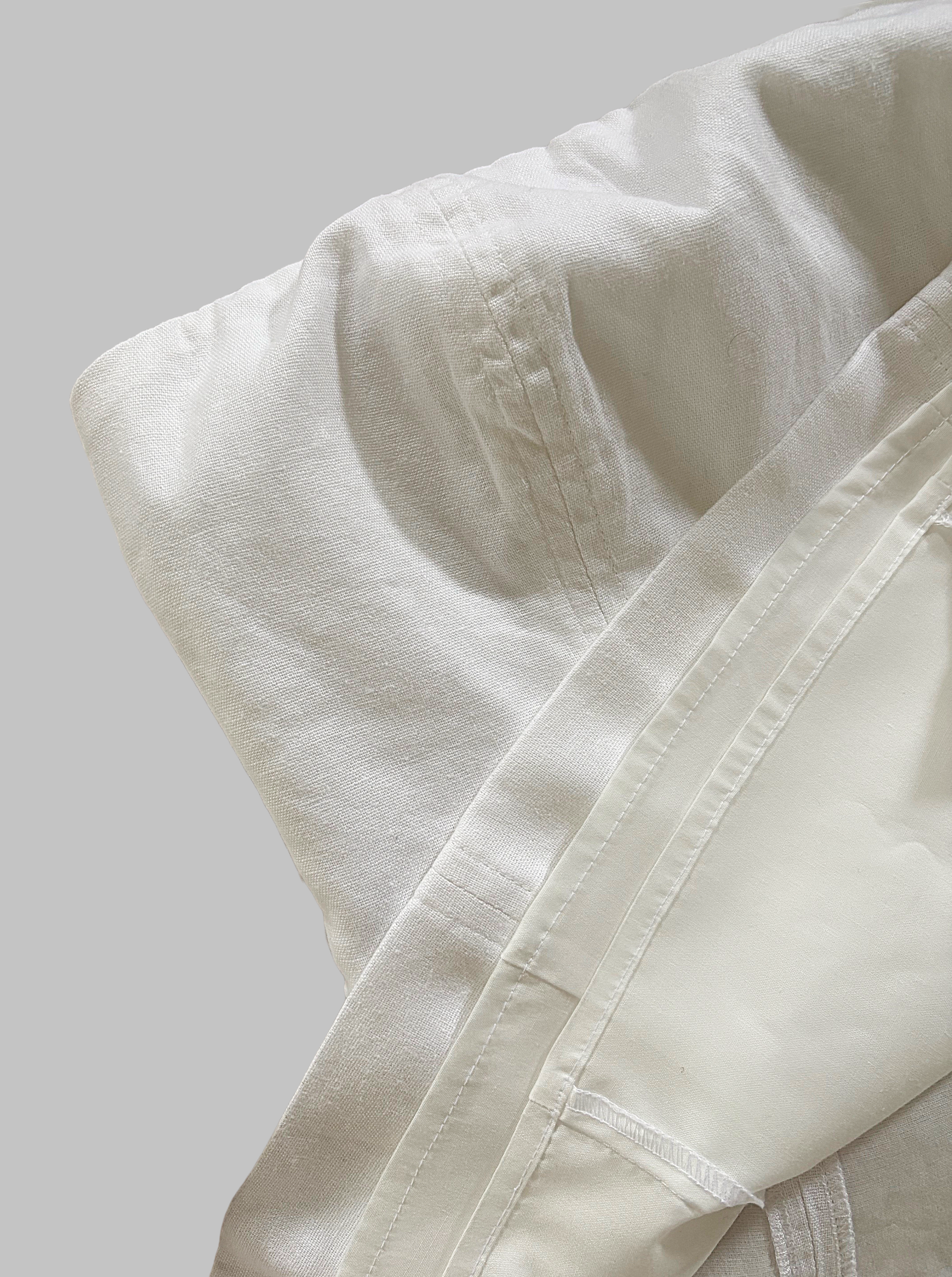 A close-up of white linen top with visible stitching and a smooth fabric texture, placed on a plain gray surface.