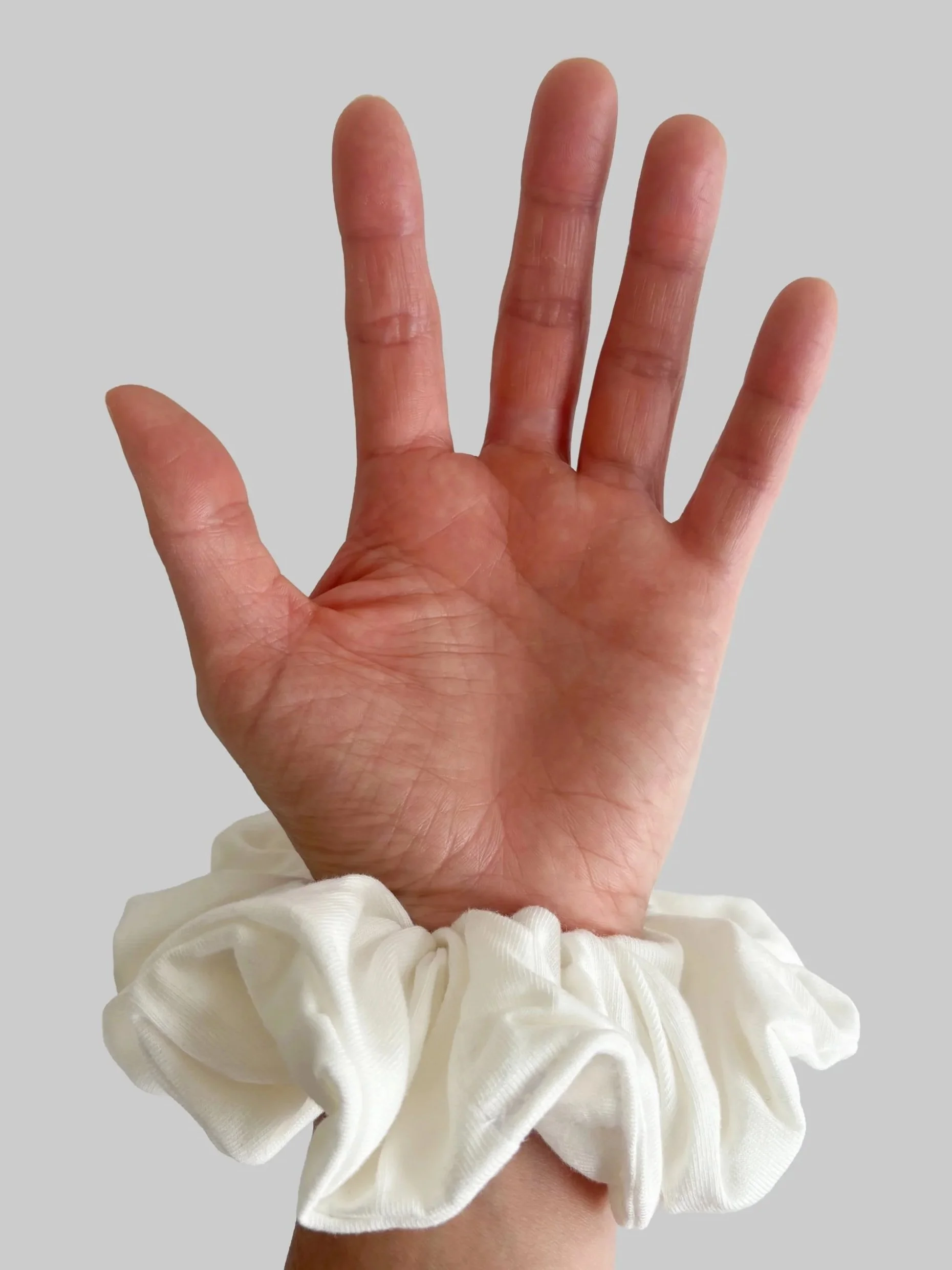 A close-up of a person's hand with five fingers extended, wearing a white ruffled wristband.