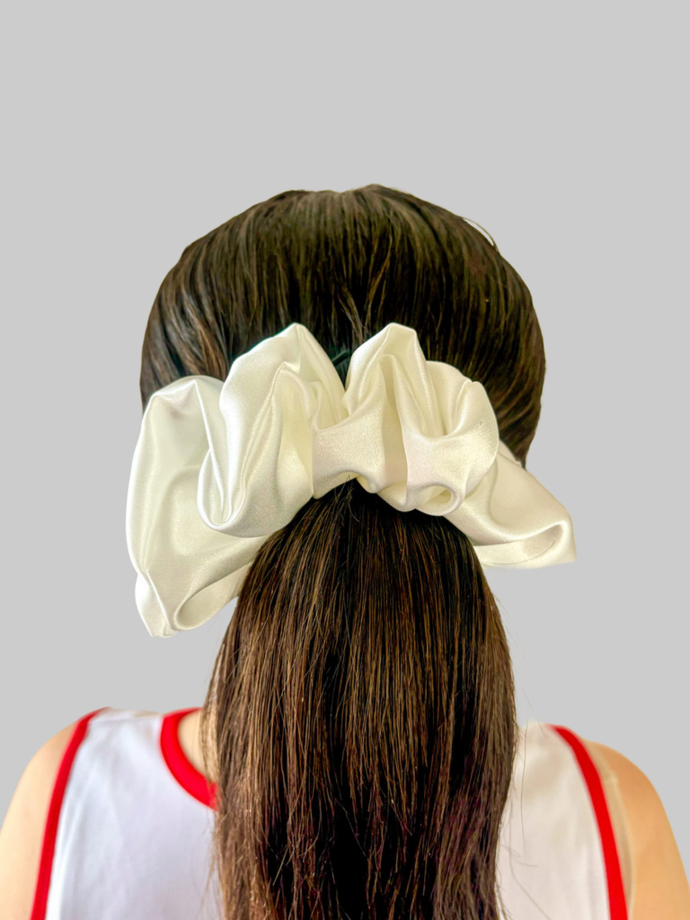 Back of a woman with long, brown hair tied with a large white satin bow, wearing a white sports jersey with red trim.