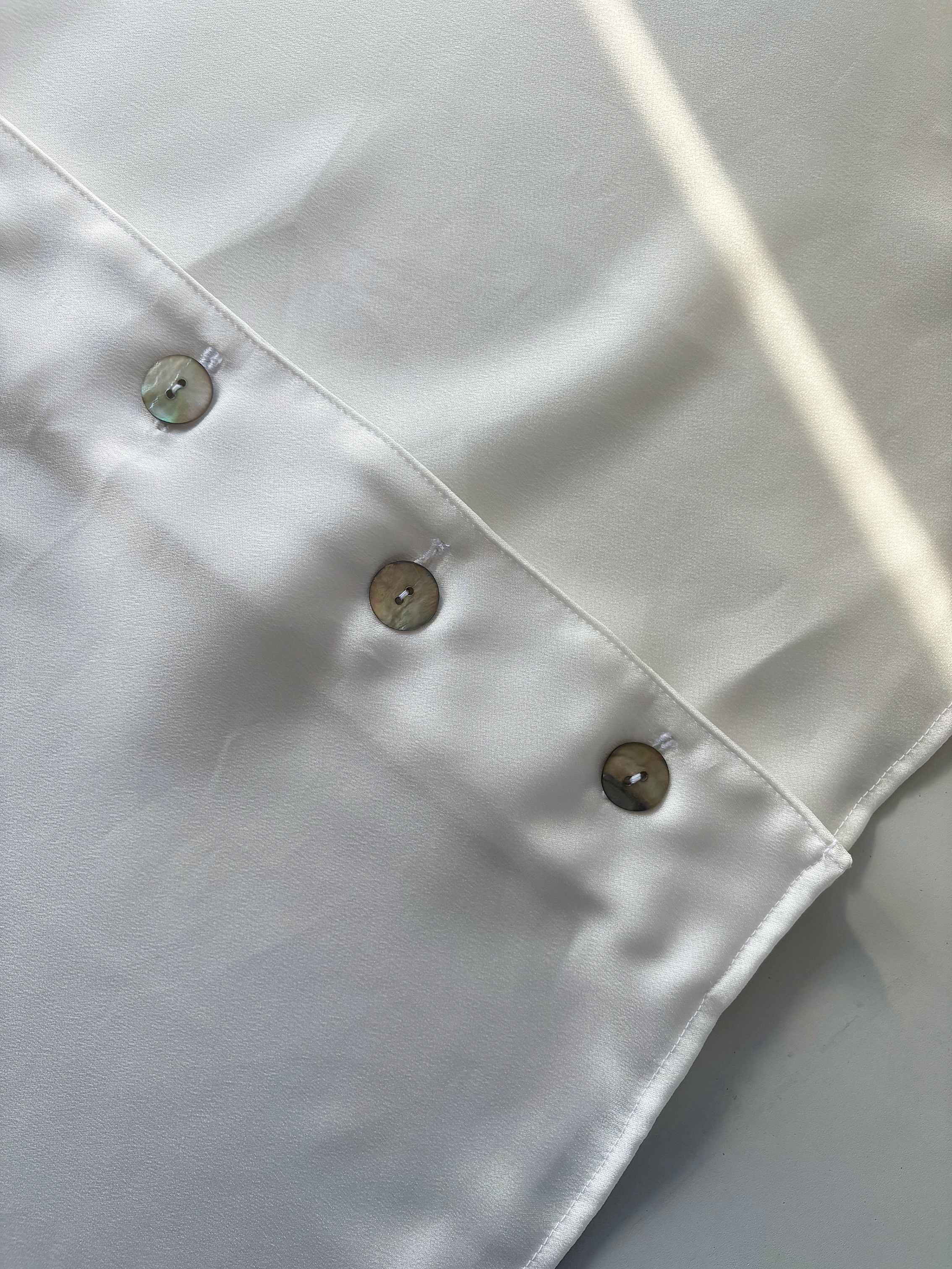Close-up of white satin dress with buttons in a row.