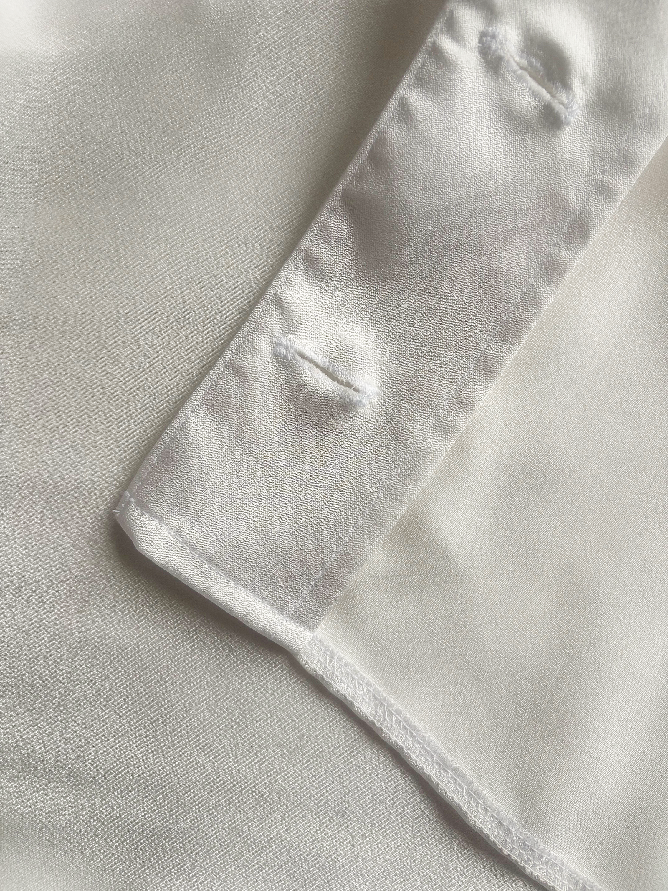 Close-up of a white satin dress showing buttonhole stand and stitching details.