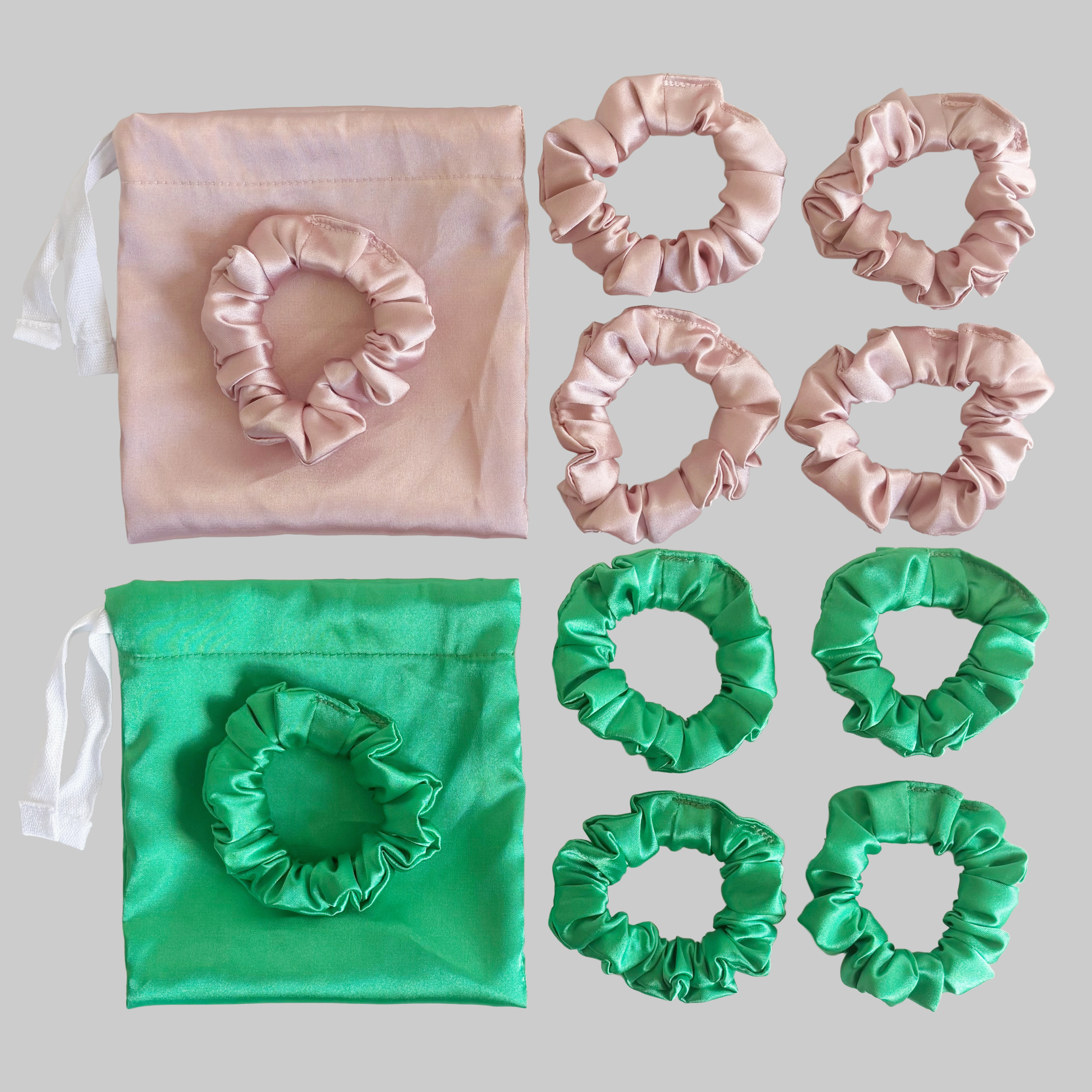 Pink satin drawstring bag with matching scrunchies and bow-shaped hair elastics, and green satin scrunchies, all arranged on a light gray background.