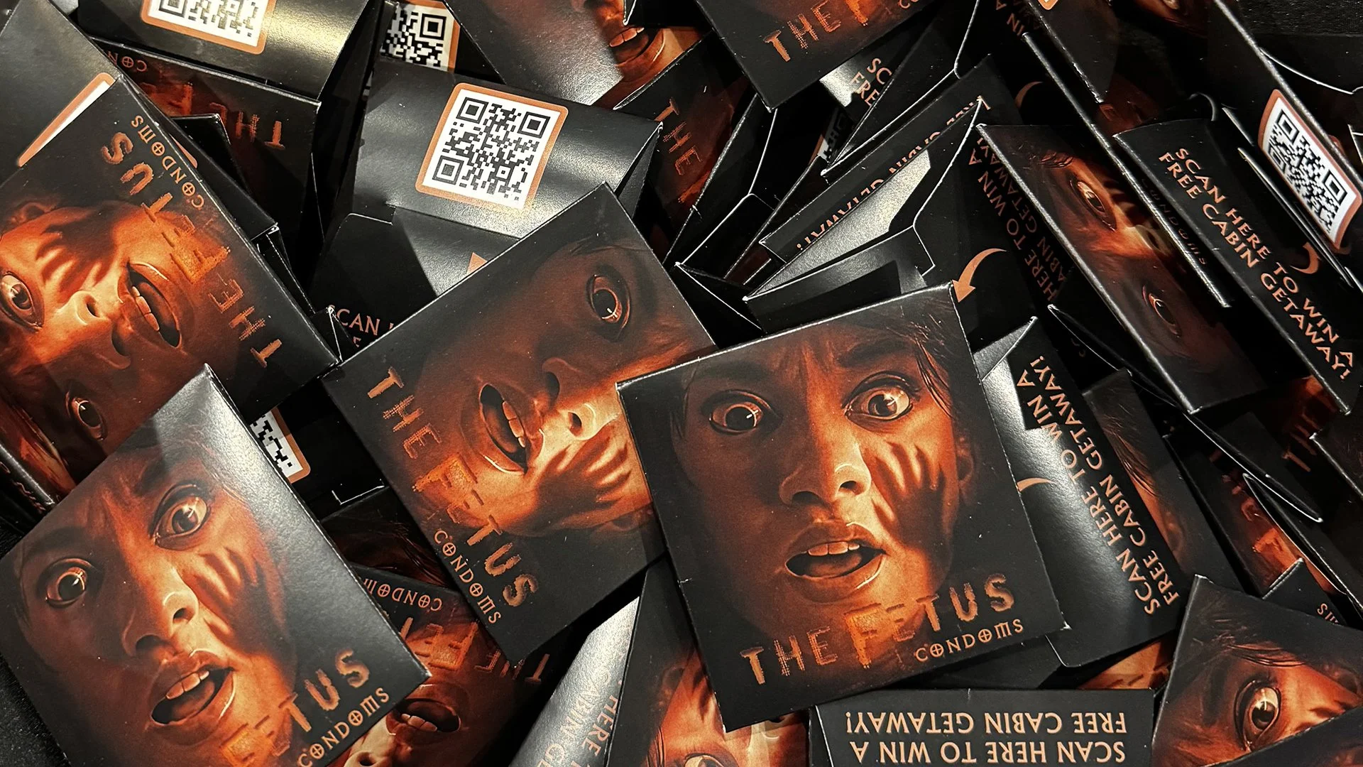 Stack of The Fetus branded condom wallets with QR codes used as guerrilla marketing giveaways at a horror convention.