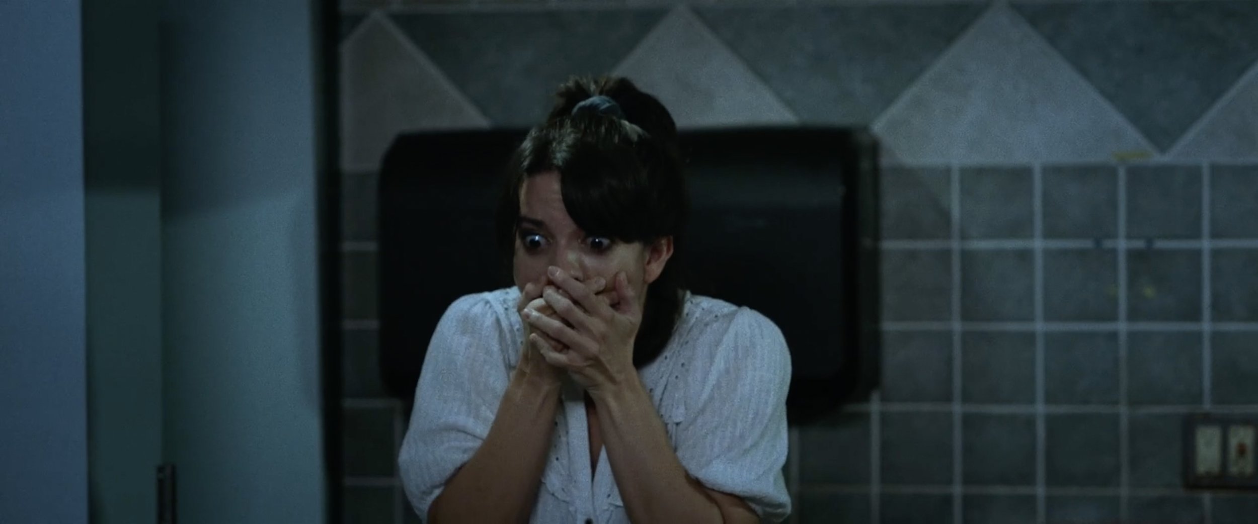 Lauren LaVera reacts in shock during a tense bathroom scene in The Fetus, illustrating how fear is used to anchor the film’s horror-comedy tone.
