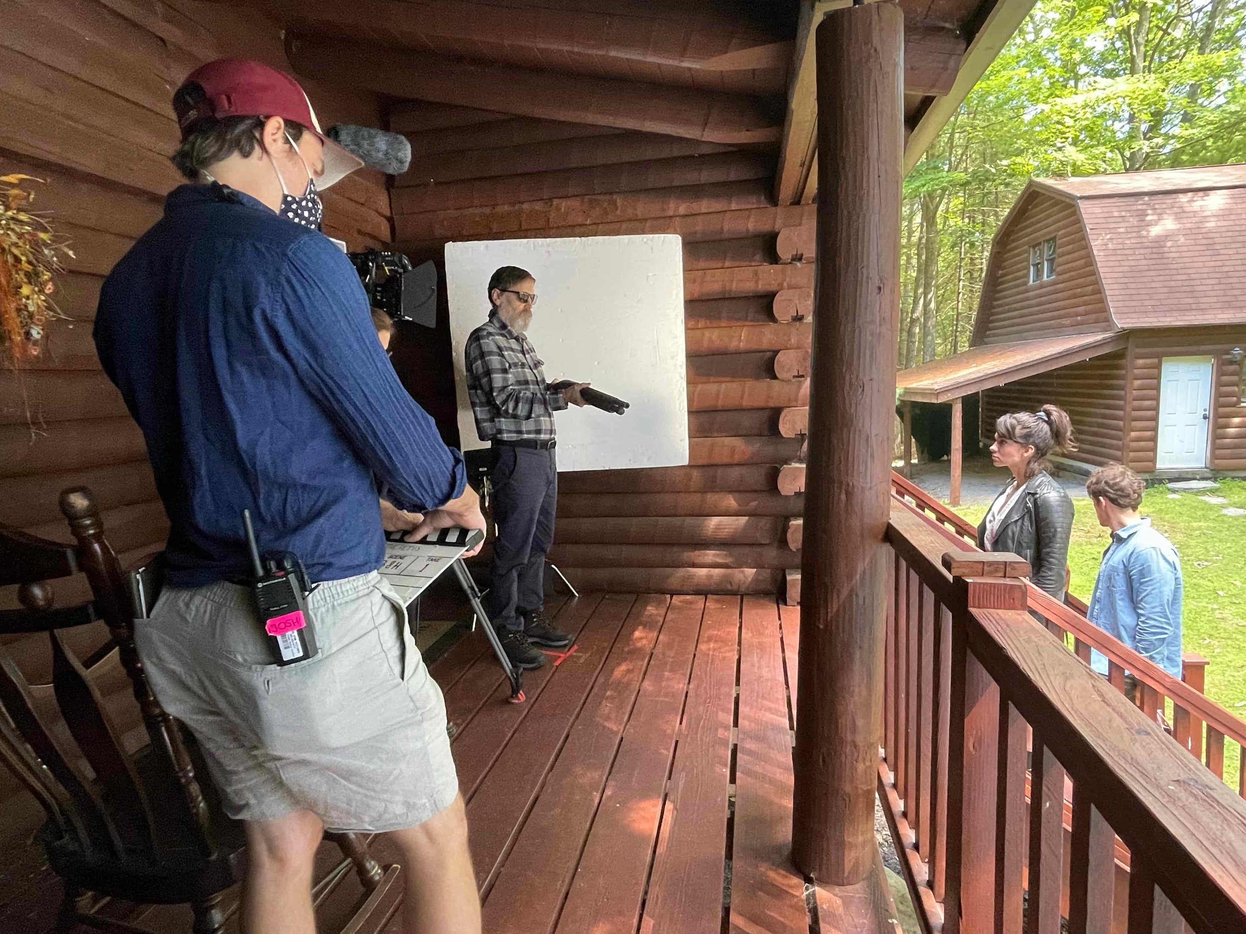Behind the scenes on the cabin porch of The Fetus — Bill Moseley holds a shotgun as 1st AD Josh Long stands by with a clapperboard, while Lauren LaVera and Julian Curtis wait in position