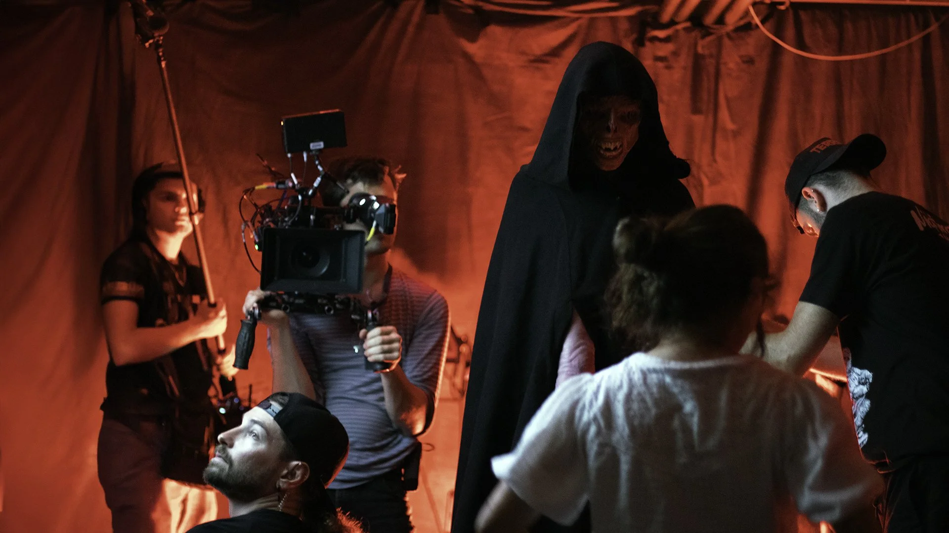 Behind-the-scenes image showing the film crew lighting and filming a cloaked creature during a practical effects scene for the indie horror film The Fetus.