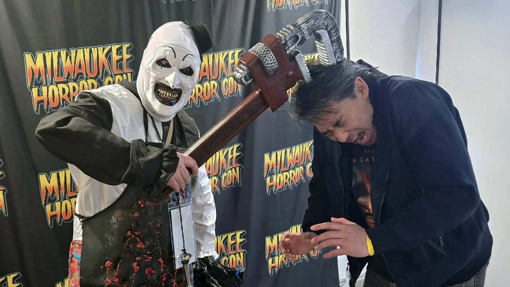 Filmmaker Joe Lam reacting as an Art the Clown cosplayer pretends to hit him with a wrench during a photo op at a horror convention.