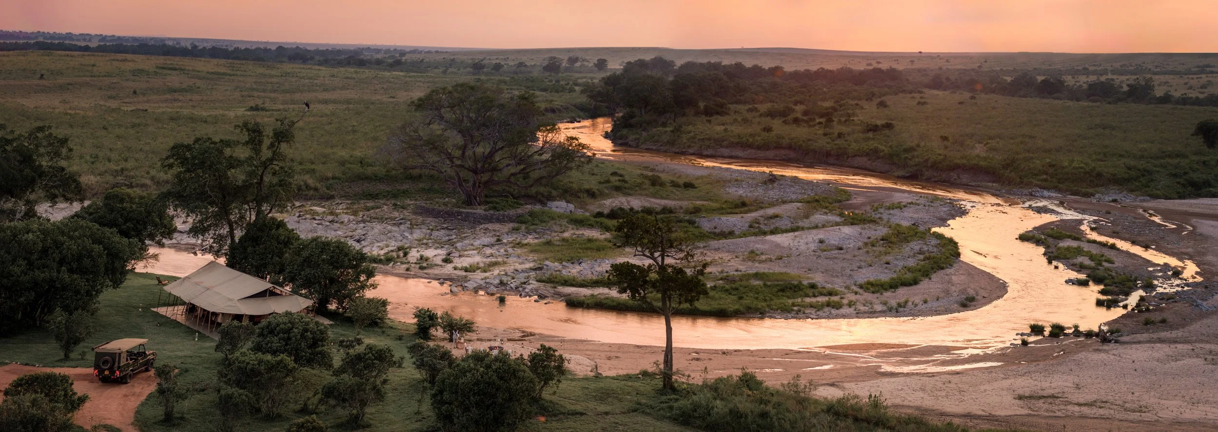 A landscape at sunset with a winding river, green trees, and a tent with a vehicle parked nearby.