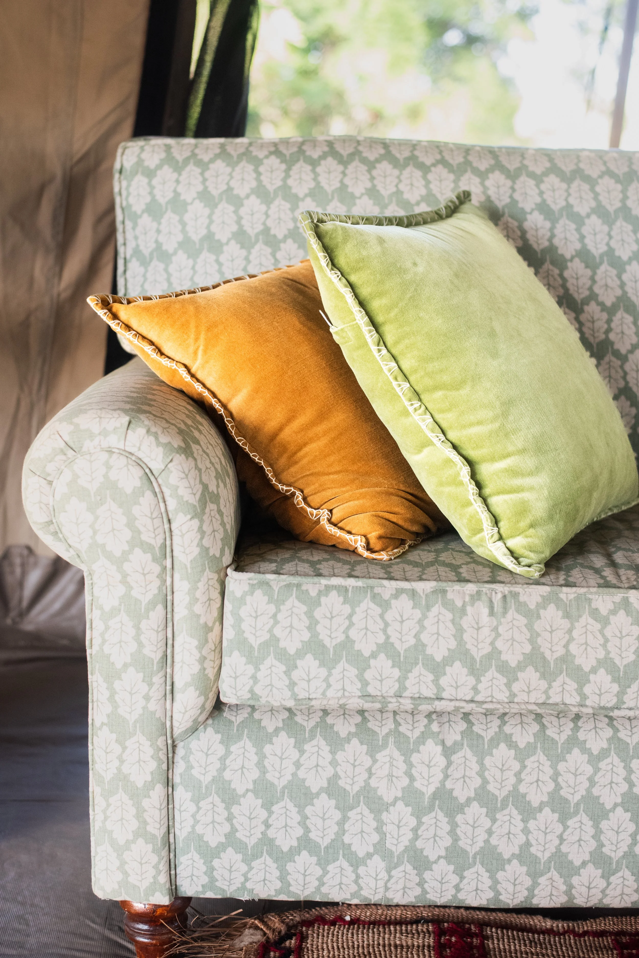 Close-up of a light-colored sofa with a leaf pattern, decorated with two velvet throw pillows in rust and lime green.