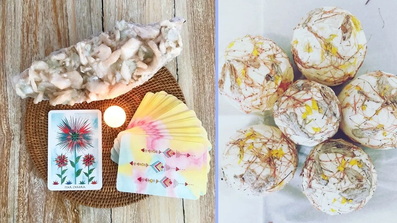 A tarot card reading setup with a deck of tarot cards, a white tea light candle, and a stone sculpture, alongside a plate of six decorative bath bombs with multicolored marbling.