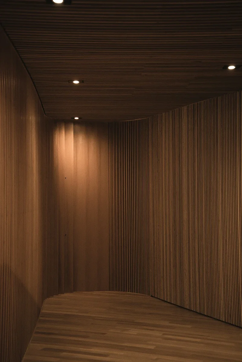 Interior corridor with wooden panel walls and ceiling, and recessed ceiling lights.