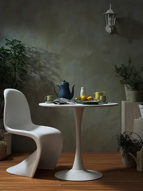 A white modern chair next to a small round white table set with a blue teapot, lemons, and cups, in a cozy room with potted plants and a lantern wall light.