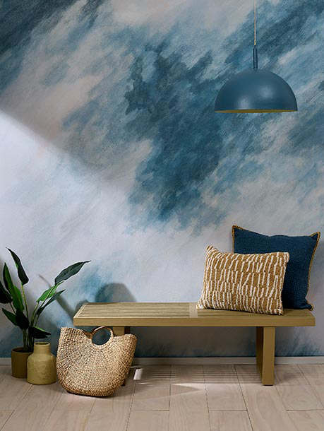 Interior space with a wooden bench, decorative pillows, a woven basket, potted plant, and a wall with a blue and white abstract mural.