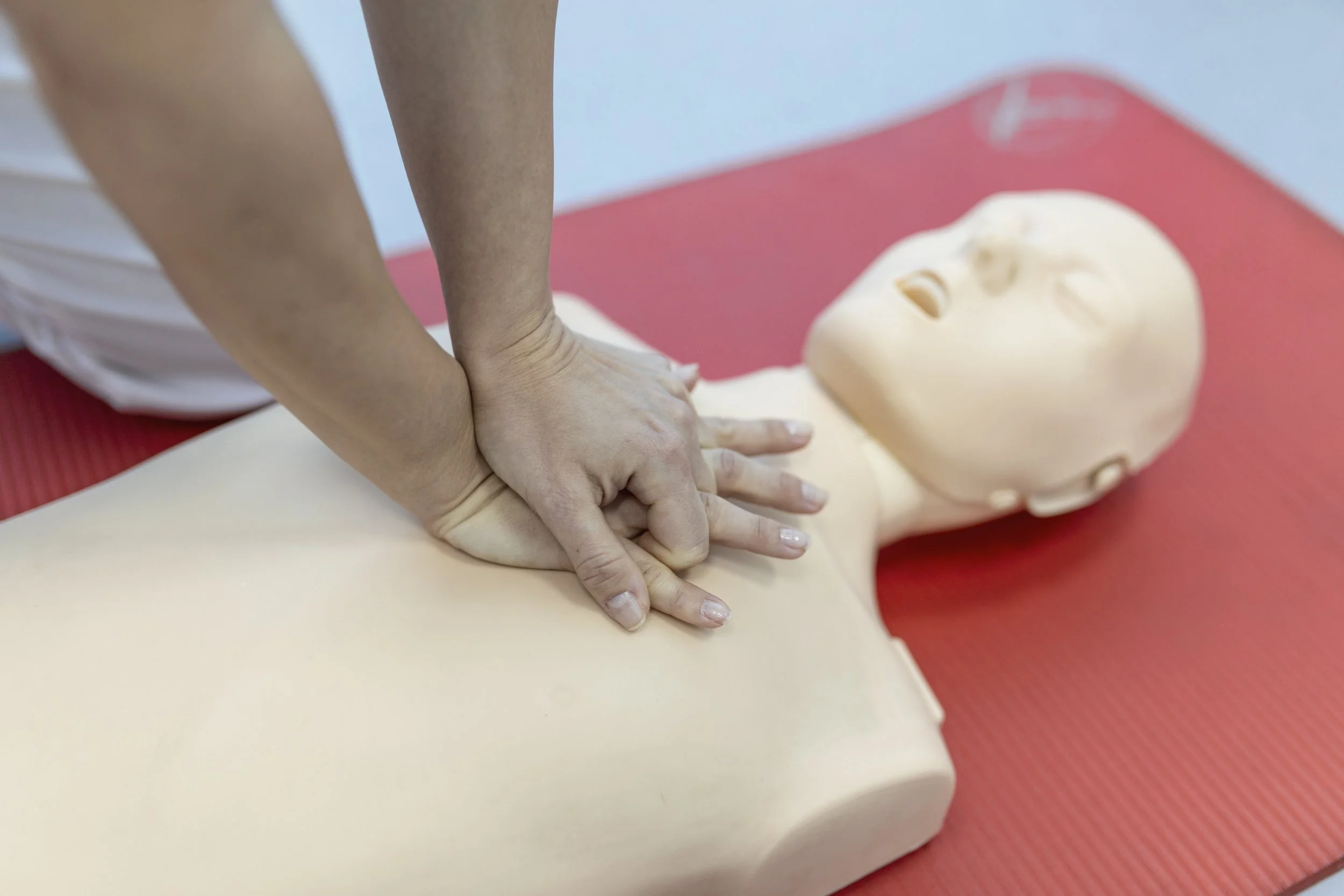 Person performing CPR on a training dummy on a red mat.