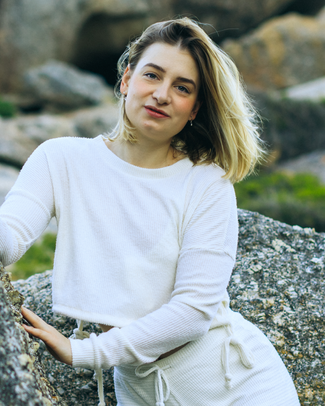 Junge Frau mit blondem Haar in weißen Kleidungsstücken im Freien auf Felsen