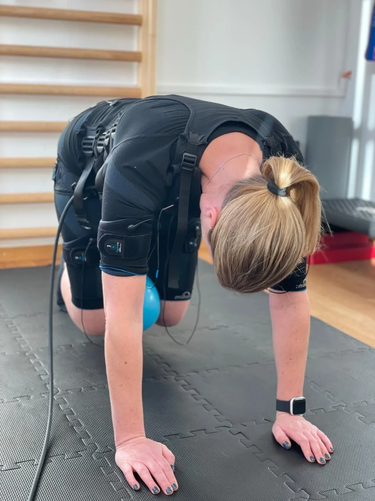 Frau trainiert auf einer Yogamatte, in der Haltung des Vierfüßlers, mit einem Fitnessball zwischen ihren Knien.