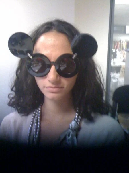 Person wearing oversized black sunglasses with round lenses and bear ears, sitting indoors.