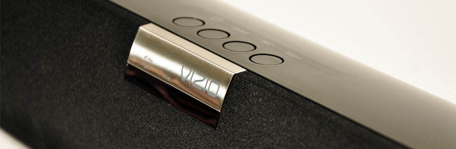 Close-up of a soundbar speaker with the brand name 'Vizio' on a metallic label, featuring control buttons on top.