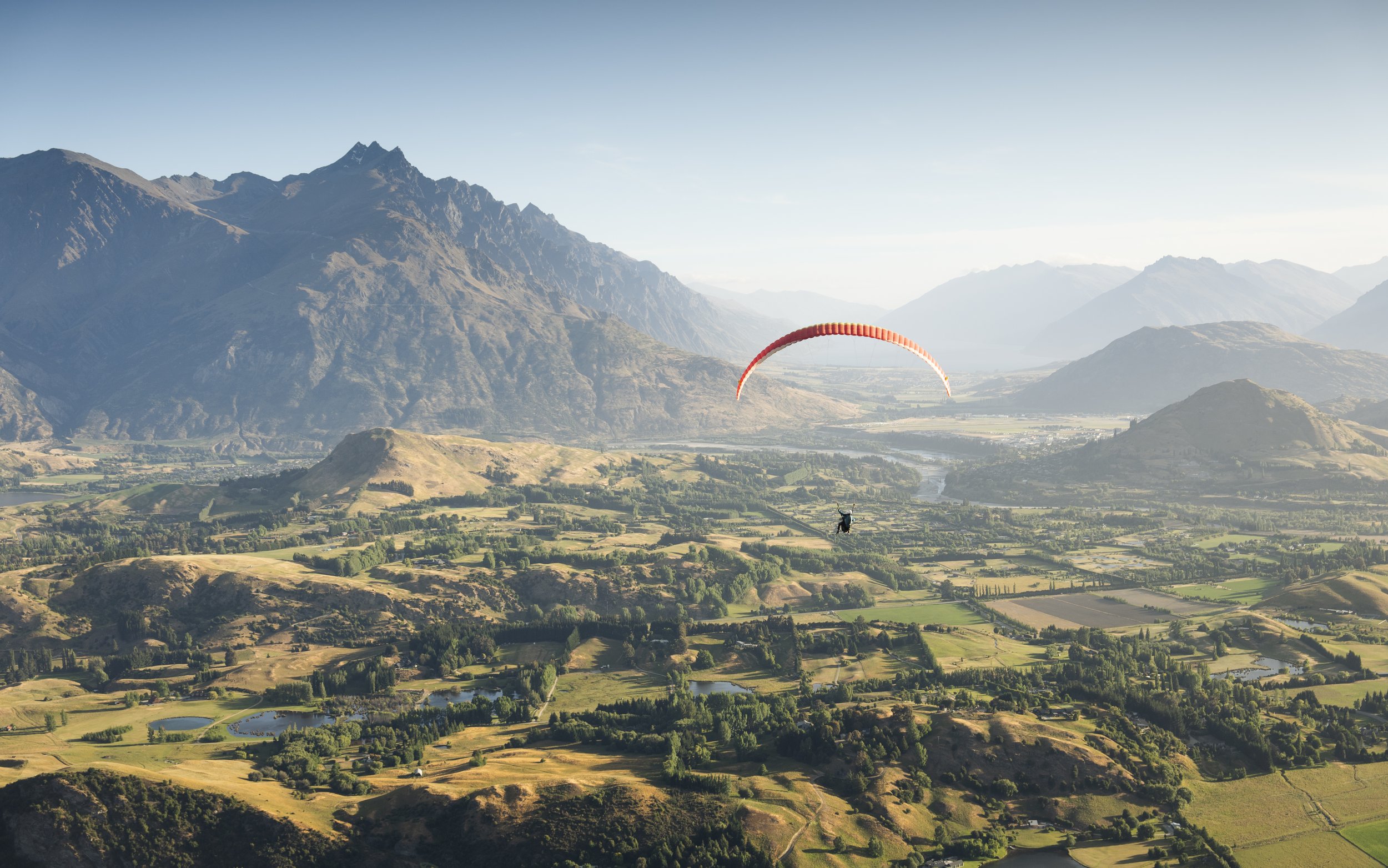A person paragliding over a lush valley with mountains in the background on a clear day.