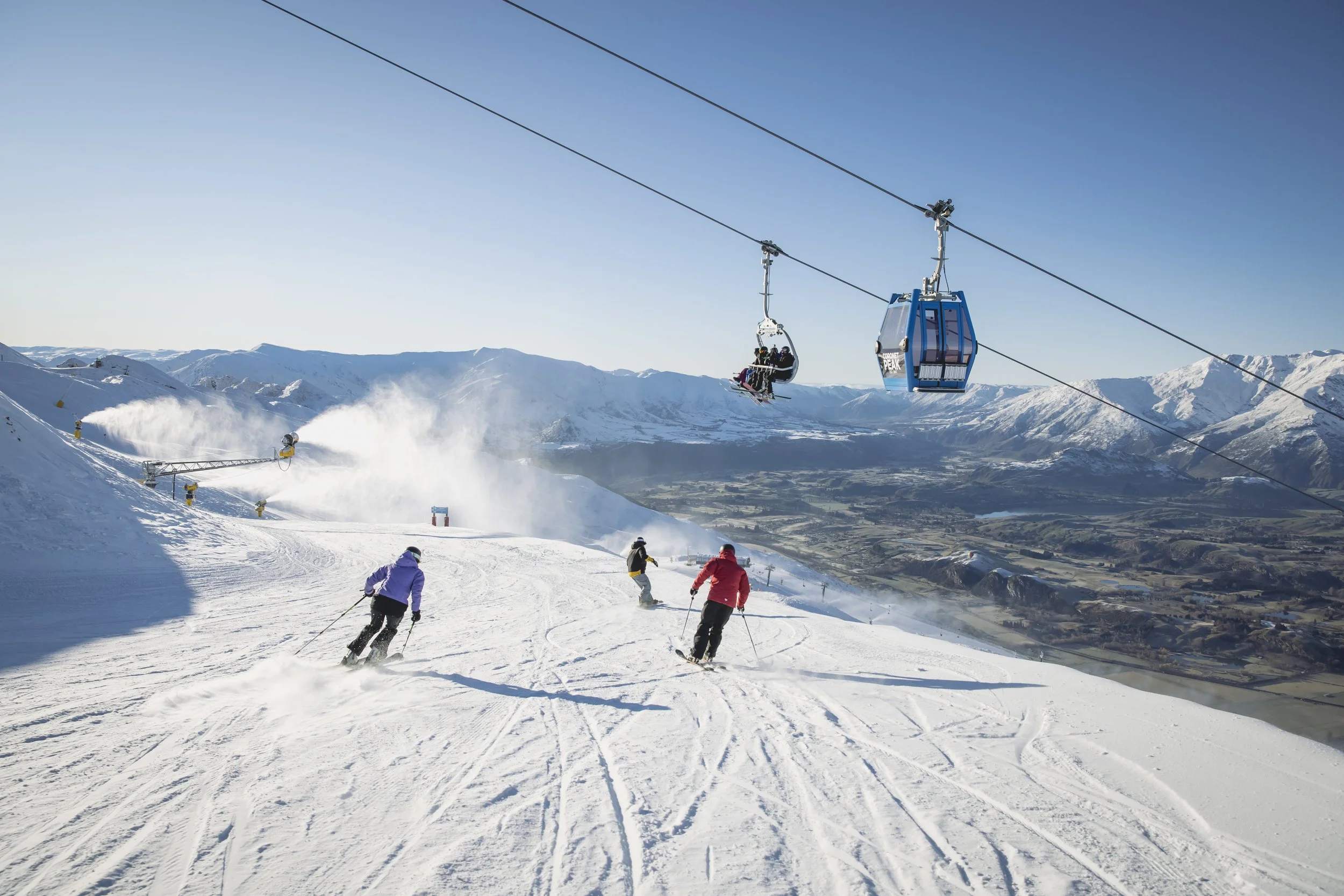 Skiers descending snow-covered mountain with alpine valley views