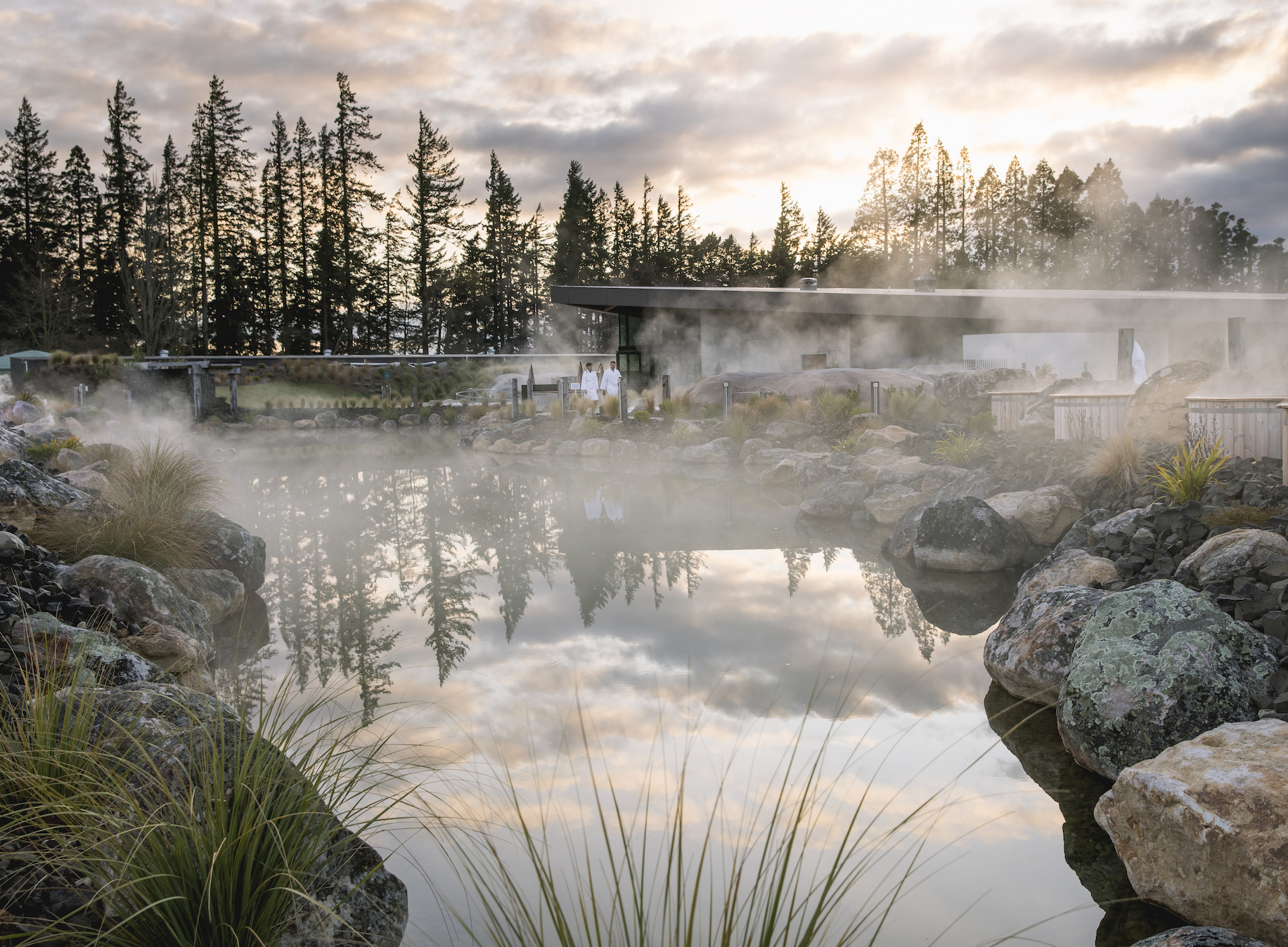 Couple in background with trees and greenery, steam rising from water from the outdoor spa and onsen v