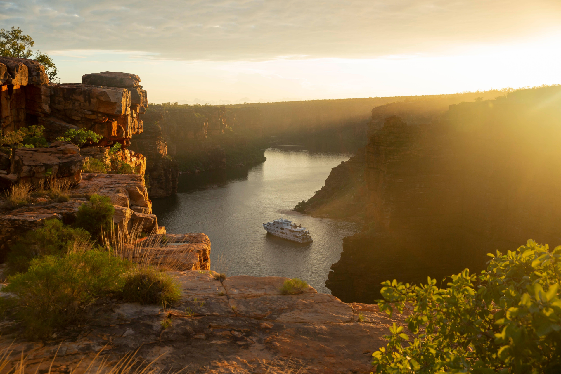 A river flowing through a canyon at sunset with a boat sailing on the water, rocky cliffs on both sides, and the sky filled with warm light.