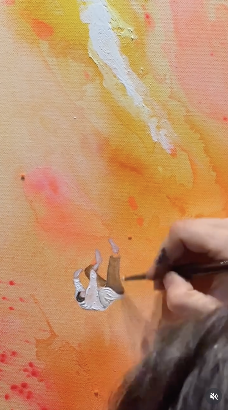 Ein Künstler malt mit Weiß auf einer farbigen Leinwand, die im Hintergrund orange, gelb und rot ist.