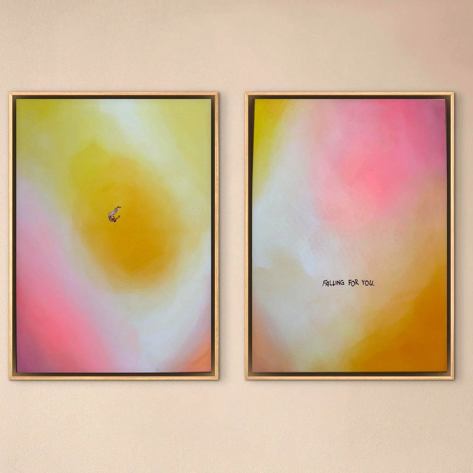 Zwei bunte, abstrakte Kunstwerke mit weichen Farbverläufen in Pastelltönen, jeweils in einem goldfarbenen Rahmen an einer hellen Wand. Das linke Bild zeigt einen kleinen, fliegenden Vogel, das rechte Bild trägt den Text "FALLING FOR YOU".