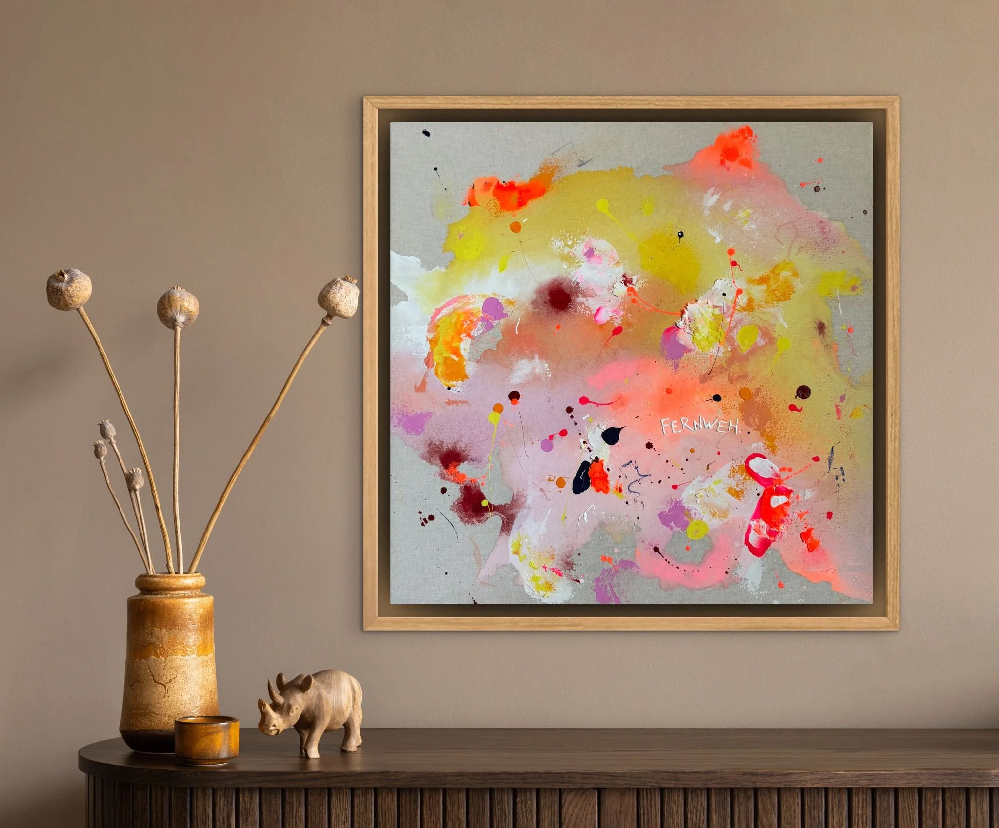 Ein modernes abstraktes Gemälde mit bunten Farben in einem Rahmen, aufgehängt an einer hellbraunen Wand. Auf einem schwarzen Möbelstück darunter befinden sich eine braune Vase mit getrockneten Pflanzen, eine kleine Kerze und eine kleine Rhinozeros-De