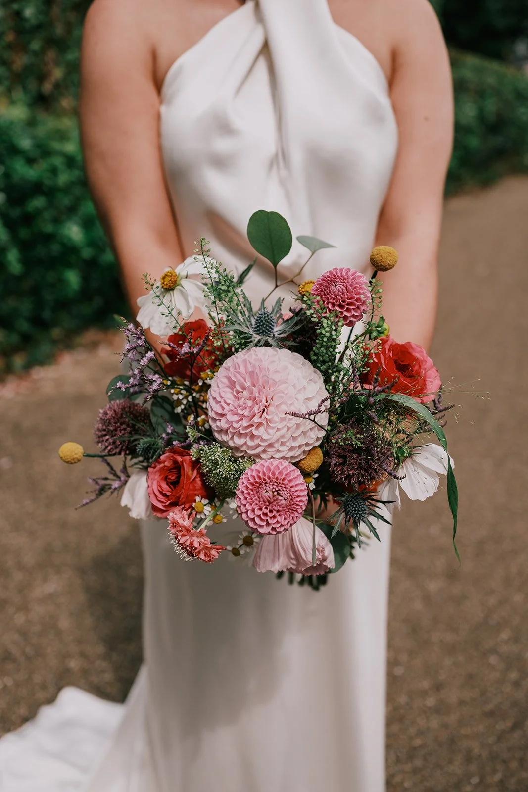 Bride holding a colorful flower bouquet including pink dahlias and roses in a white dress.